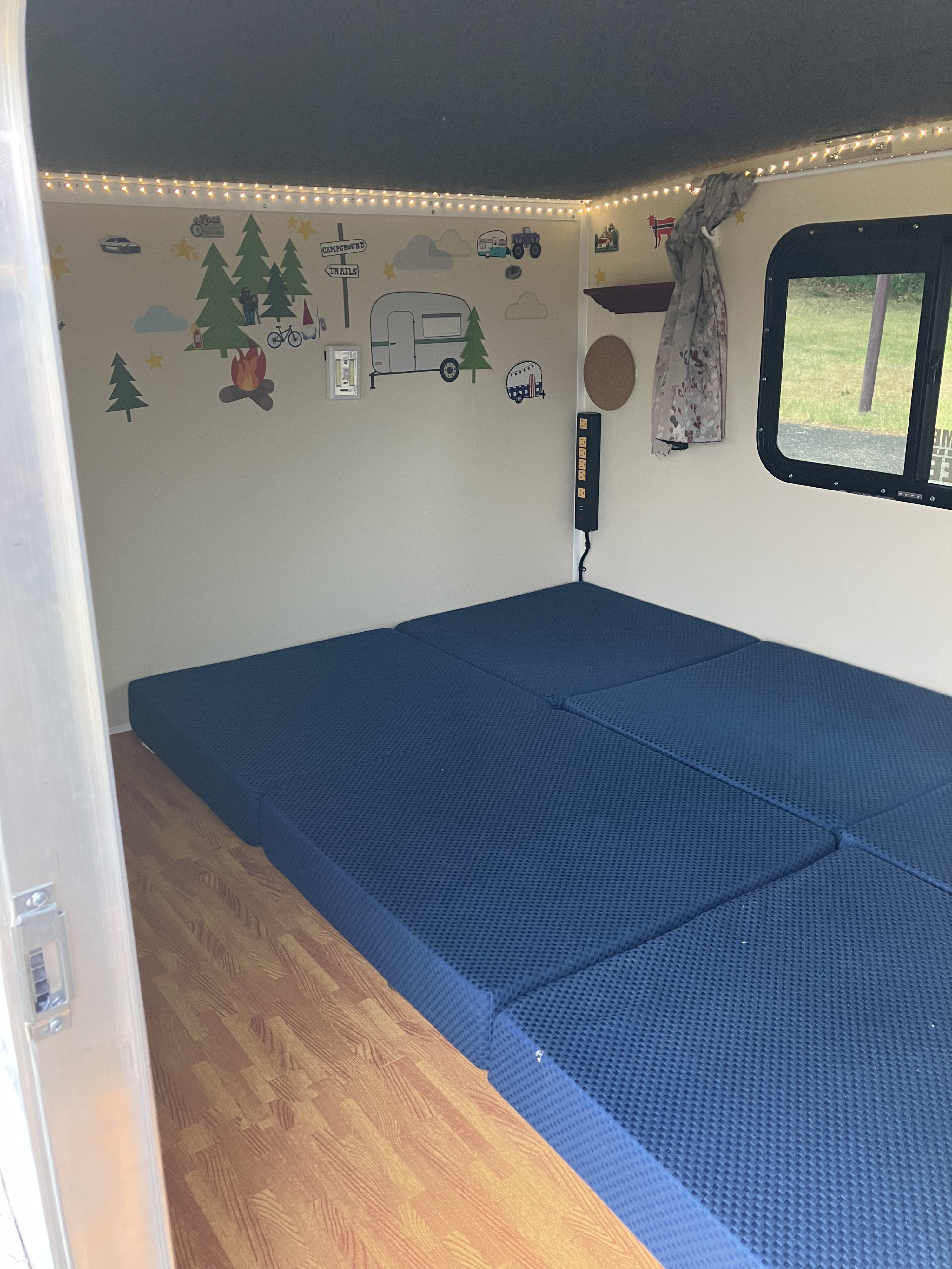 Inside an RV rental: decorated walls, comfy blue modular bed, string lights, and a window view. Perfect for camping trips.. Runaway rangerunner 2021