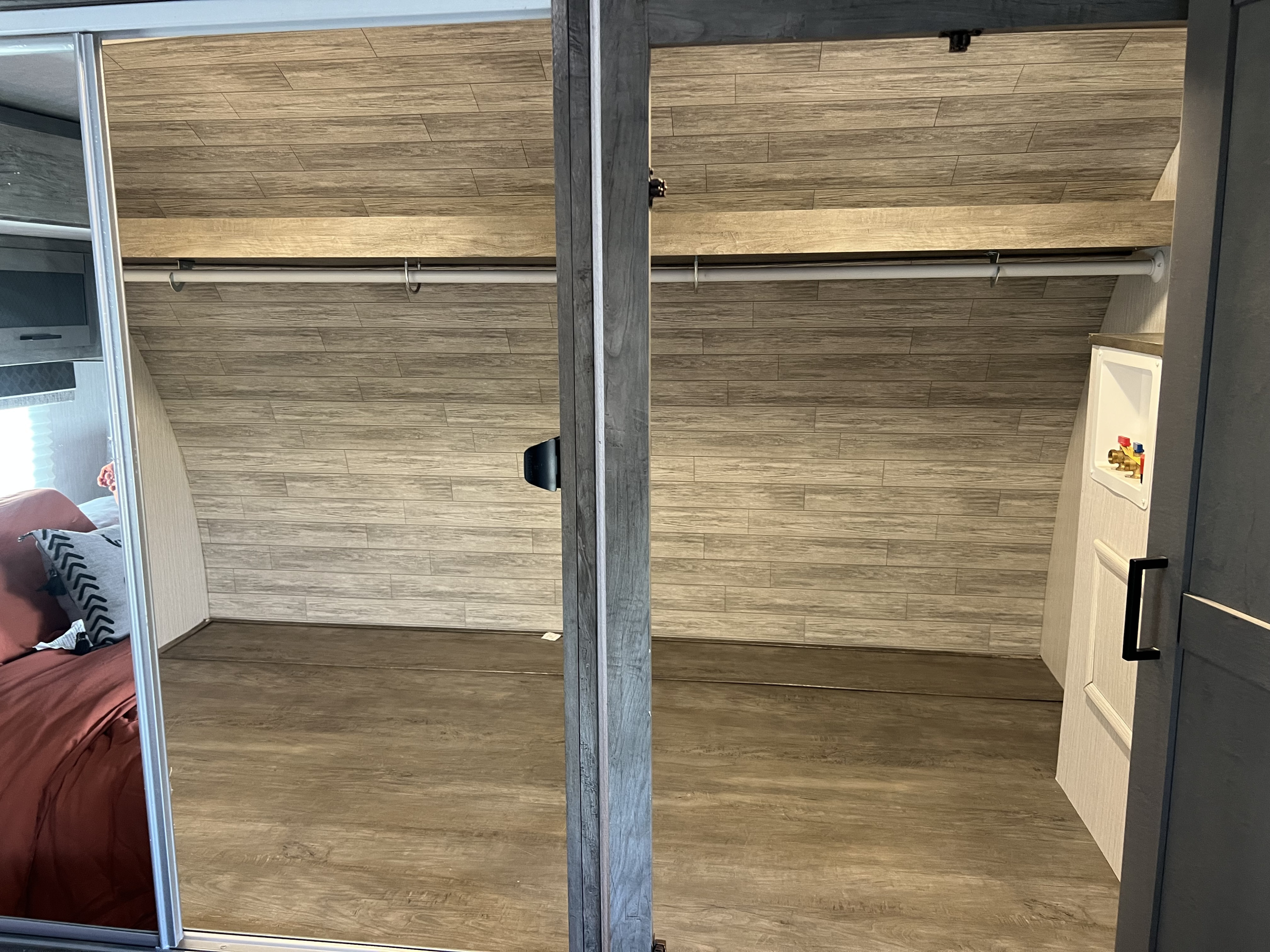 RV rental closet with wood-look walls, clothes rod, and washer hookups, plus a bedroom reflection.. Heartland RVs North Trail 2021