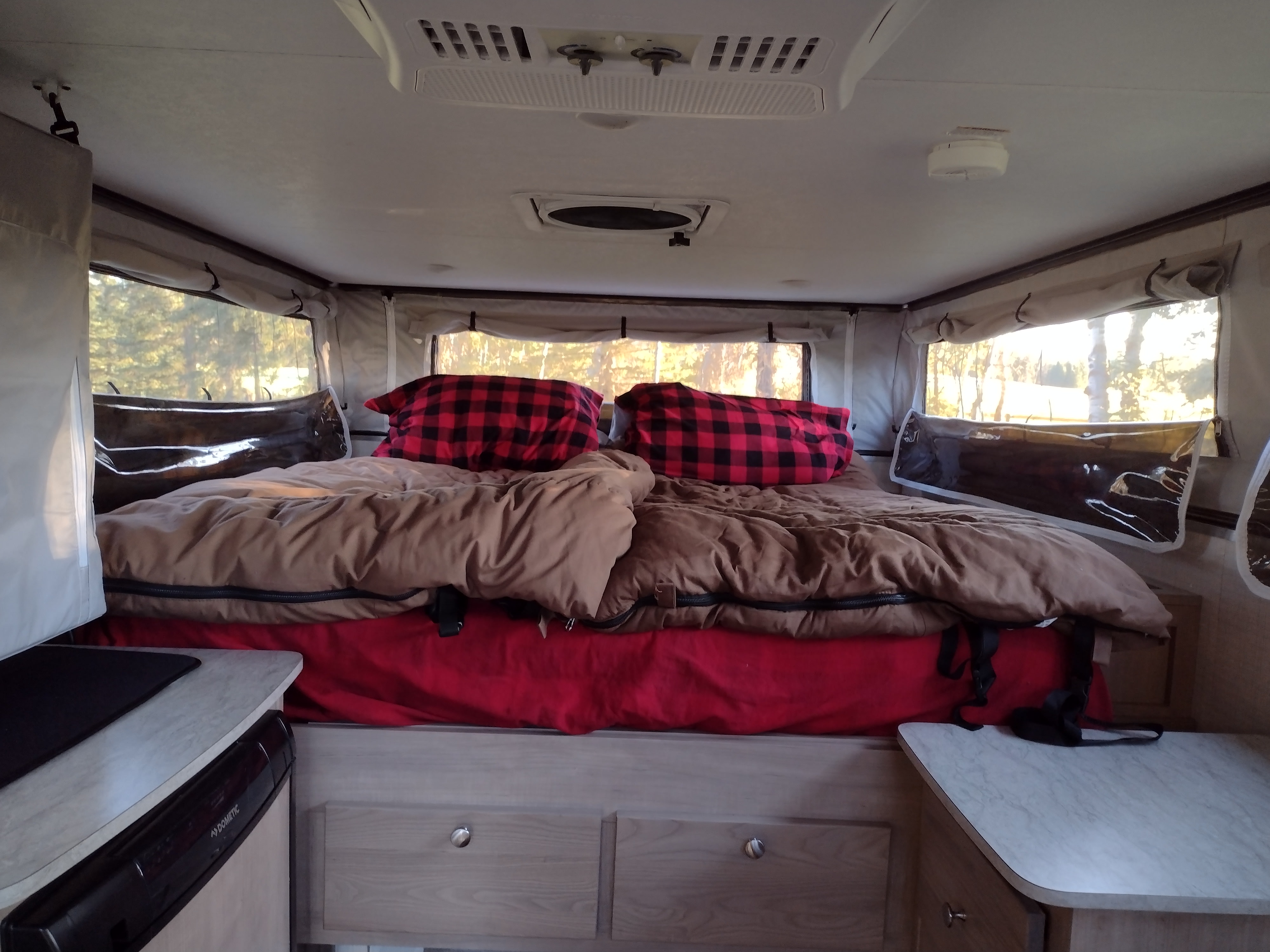 Inside a cozy RV rental: a bed with buffalo check pillows & bright windows. Perfect for camping!. Palomino Backpack Edition 2023