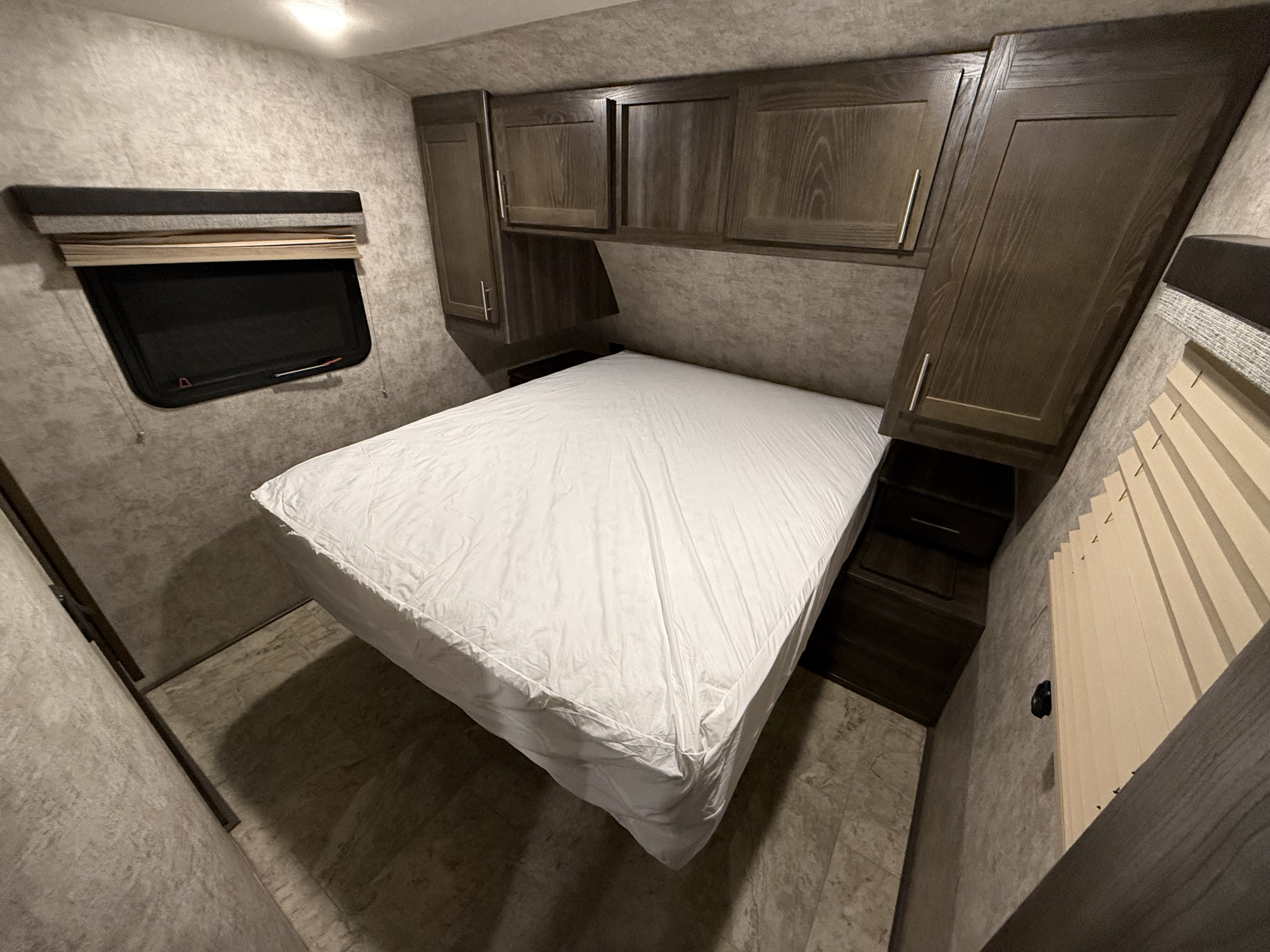 Inside an RV rental, discover this cozy bedroom with a bed, practical overhead cabinets, and a side window.. Highland Ridge RV Light 2018
