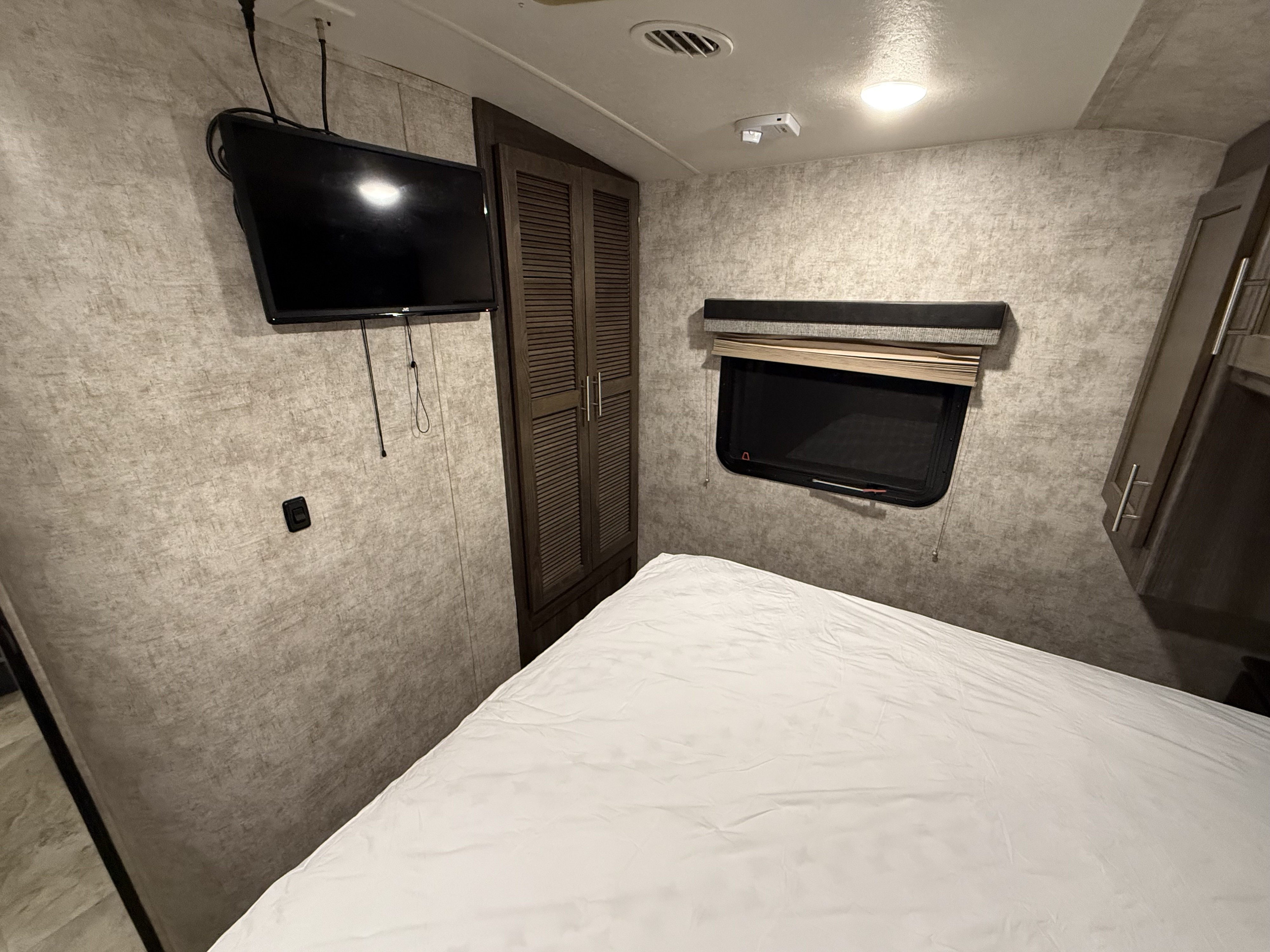 RV rental bedroom interior with a white-sheeted bed, wall-mounted TV, tall wardrobe, and window.. Highland Ridge RV Light 2018