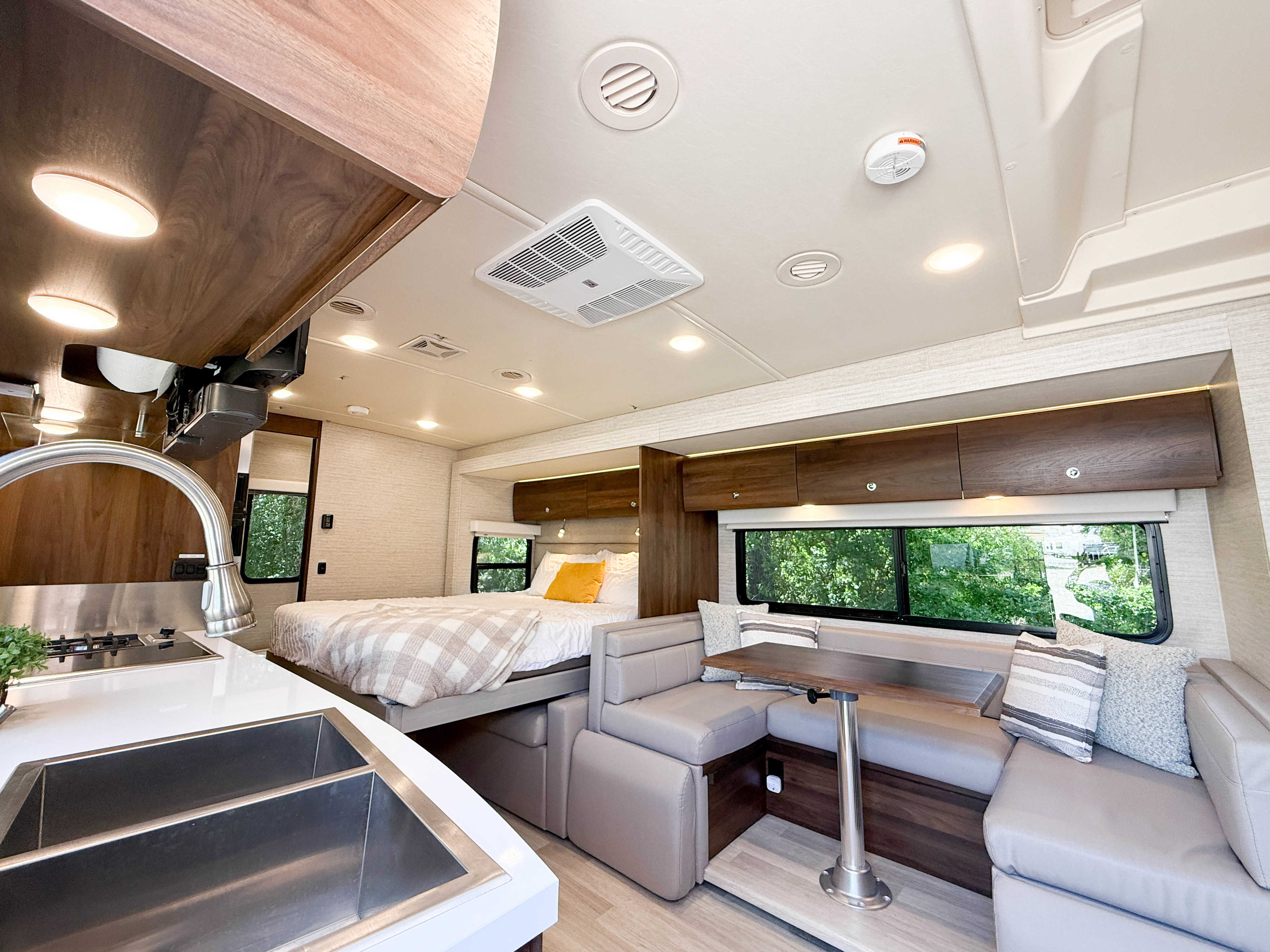 Inside this modern RV rental: a comfortable bedroom, L-shaped lounge with dining table, and a functional kitchen.. Winnebago View 2023