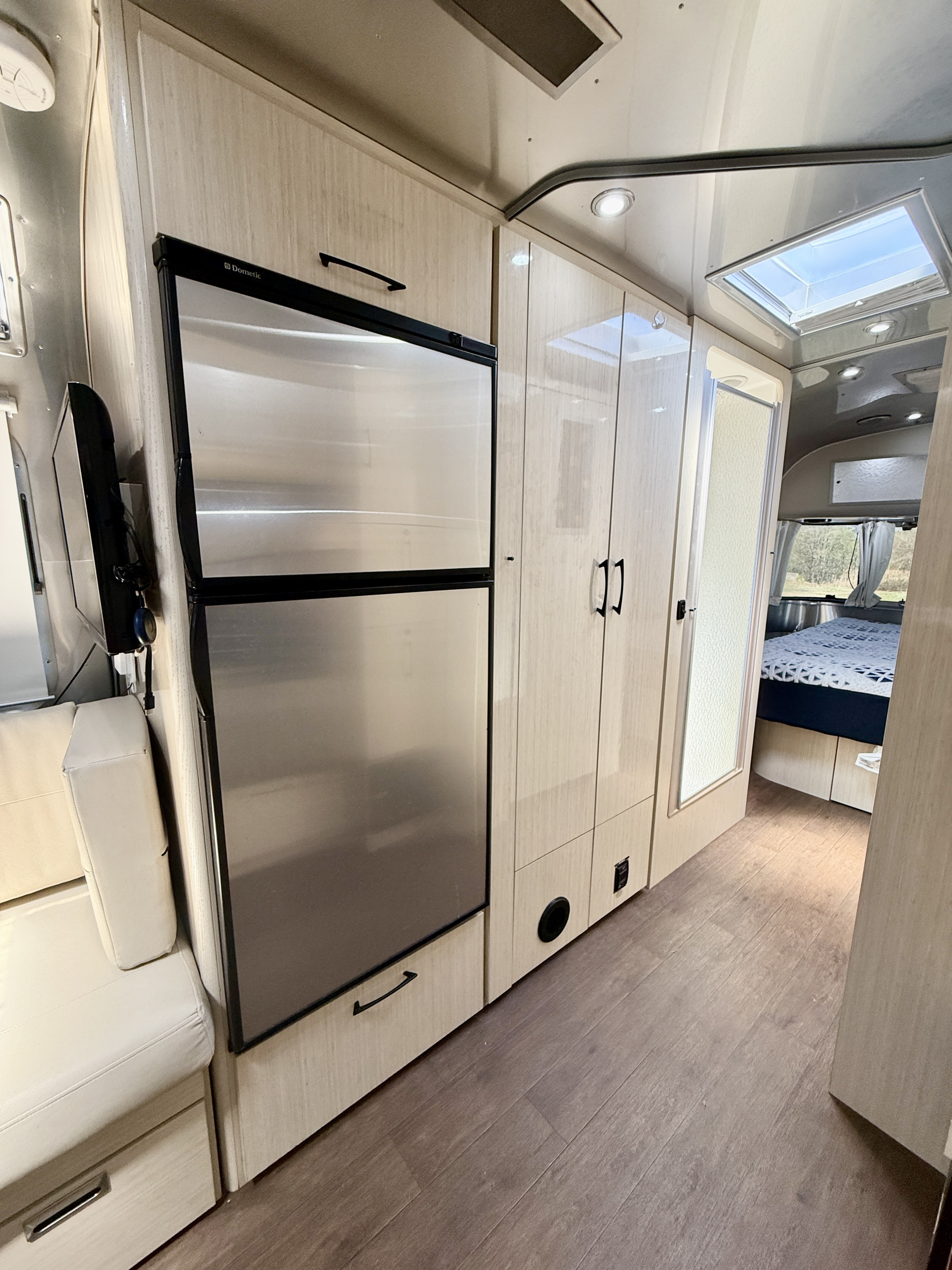 Bright and modern RV rental interior featuring a stainless fridge, ample cabinetry, shower, and a cozy bedroom.. Airstream 27FBINT 2017