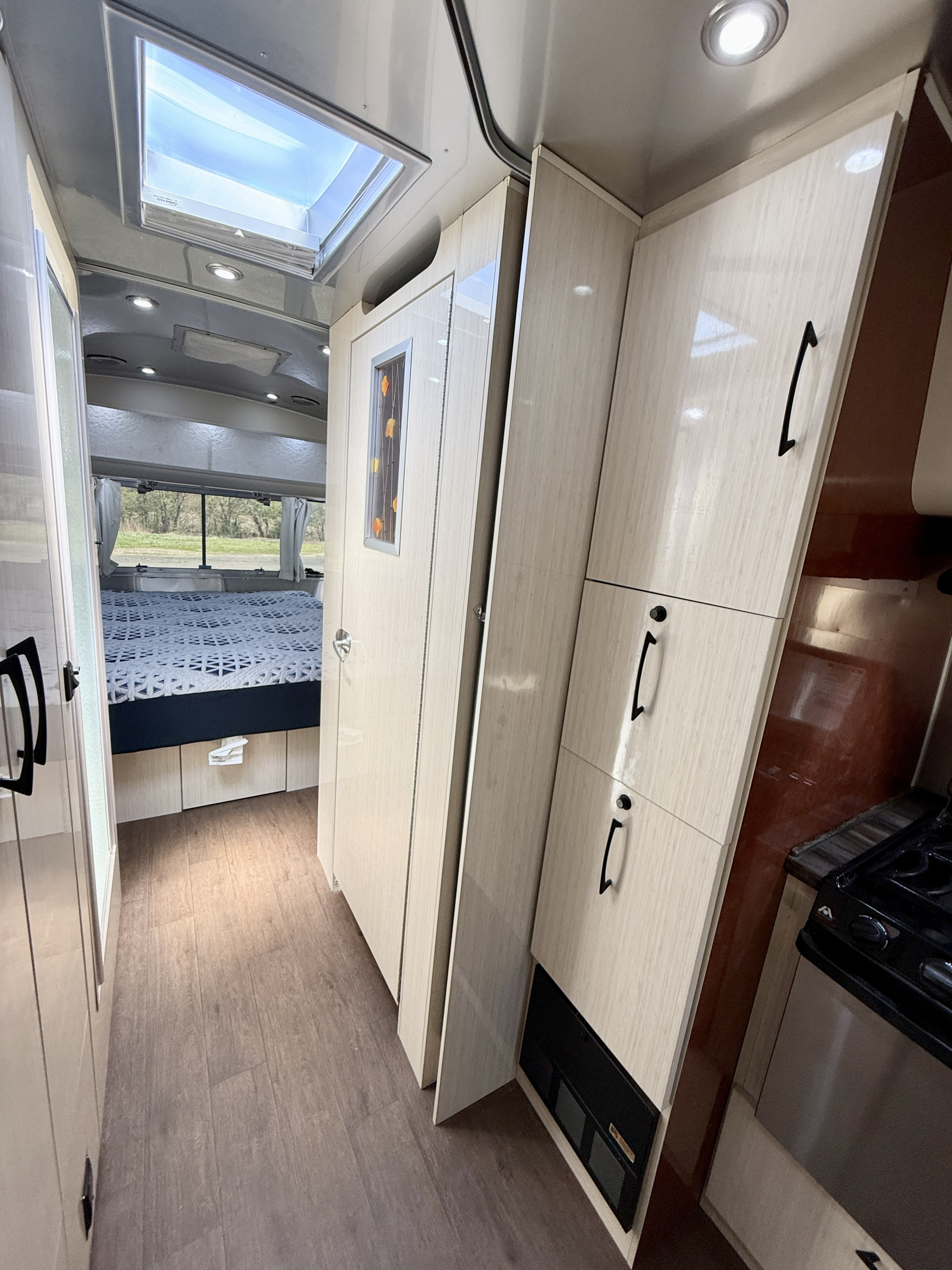 RV rental interior: bright hallway, bedroom, kitchen area, light wood cabinets, and skylight.. Airstream 27FBINT 2017