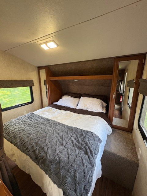 Cozy RV rental bedroom featuring a comfortable queen bed, mirrored wardrobes, overhead storage, and side windows.. Forest River Wildwood X-Lite 2015