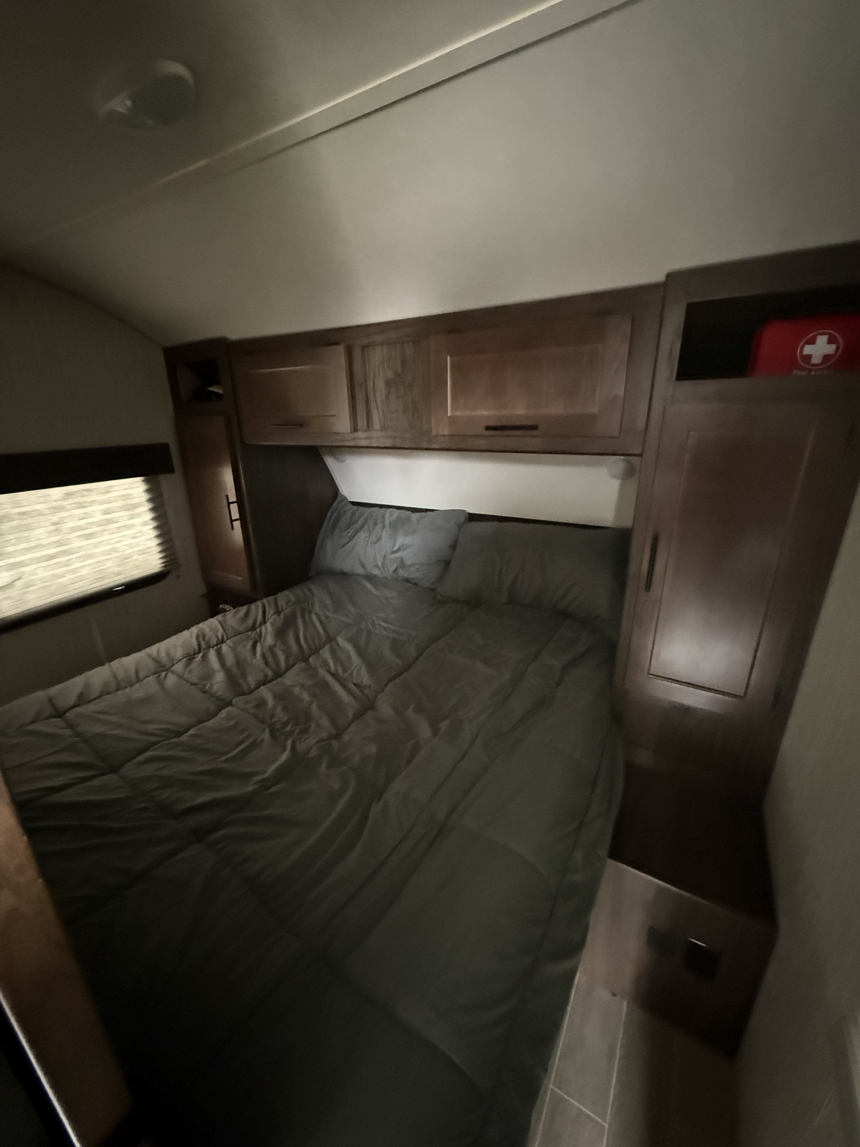 Inside an RV rental bedroom: grey bed, overhead cabinets, window, and a visible first-aid kit. Ready for adventures!. Forest River Cherokee Grey Wolf 2020