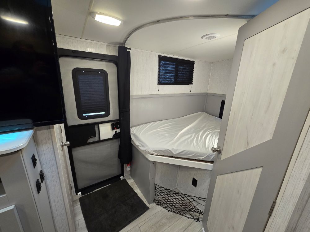 Inside this RV rental, discover a compact bedroom with a comfortable bed, window, TV, and door for easy access.. Heartland North Trail 29BHP 2022