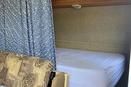 Inside an RV rental, showing a sleeping area with a clean mattress, a patterned sofa, and a privacy curtain.. Gulf Stream Ameri-Lite 2009