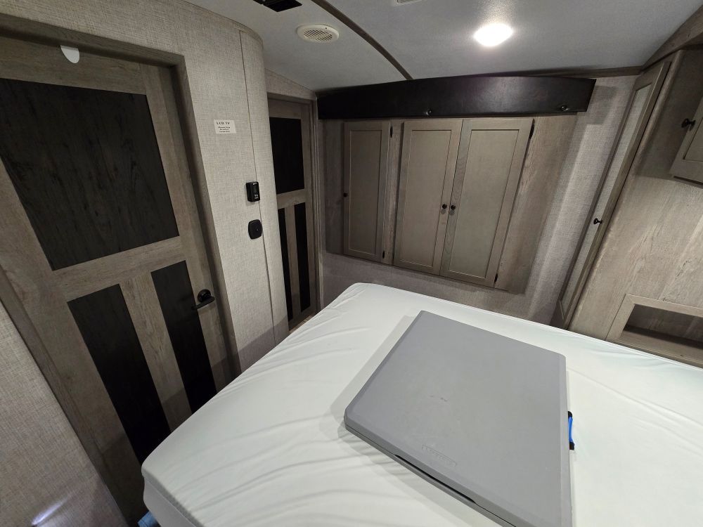 Inside an **RV rental** bedroom: a cozy bed with a portable table, built-in cabinets, and a side door. Compact living space.. Keystone Outback 335CG 2021