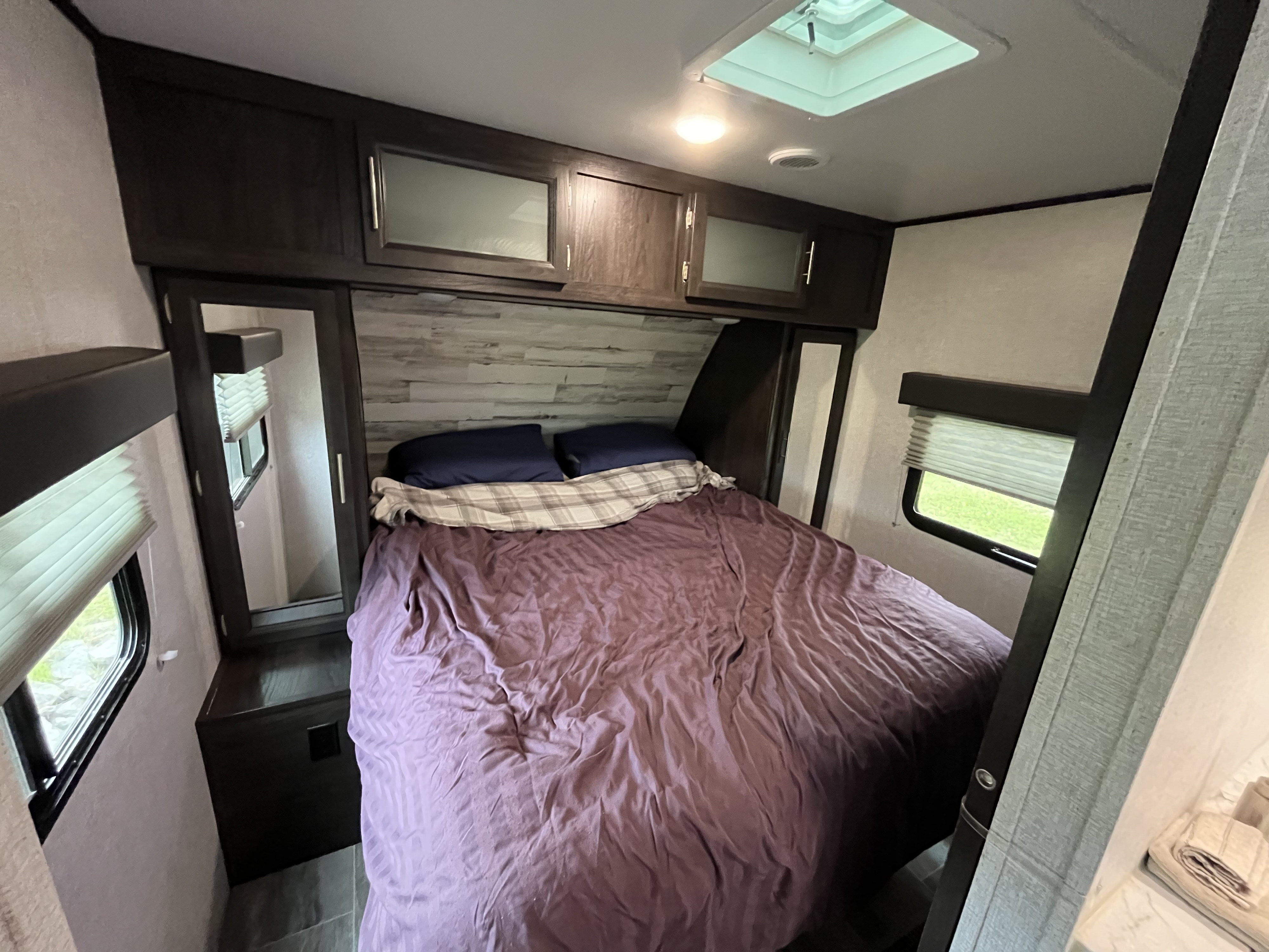 Spacious RV rental bedroom featuring a cozy bed with purple bedding, overhead cabinets, and windows.. Dutchmen Kodiak Ultra Lite 2020