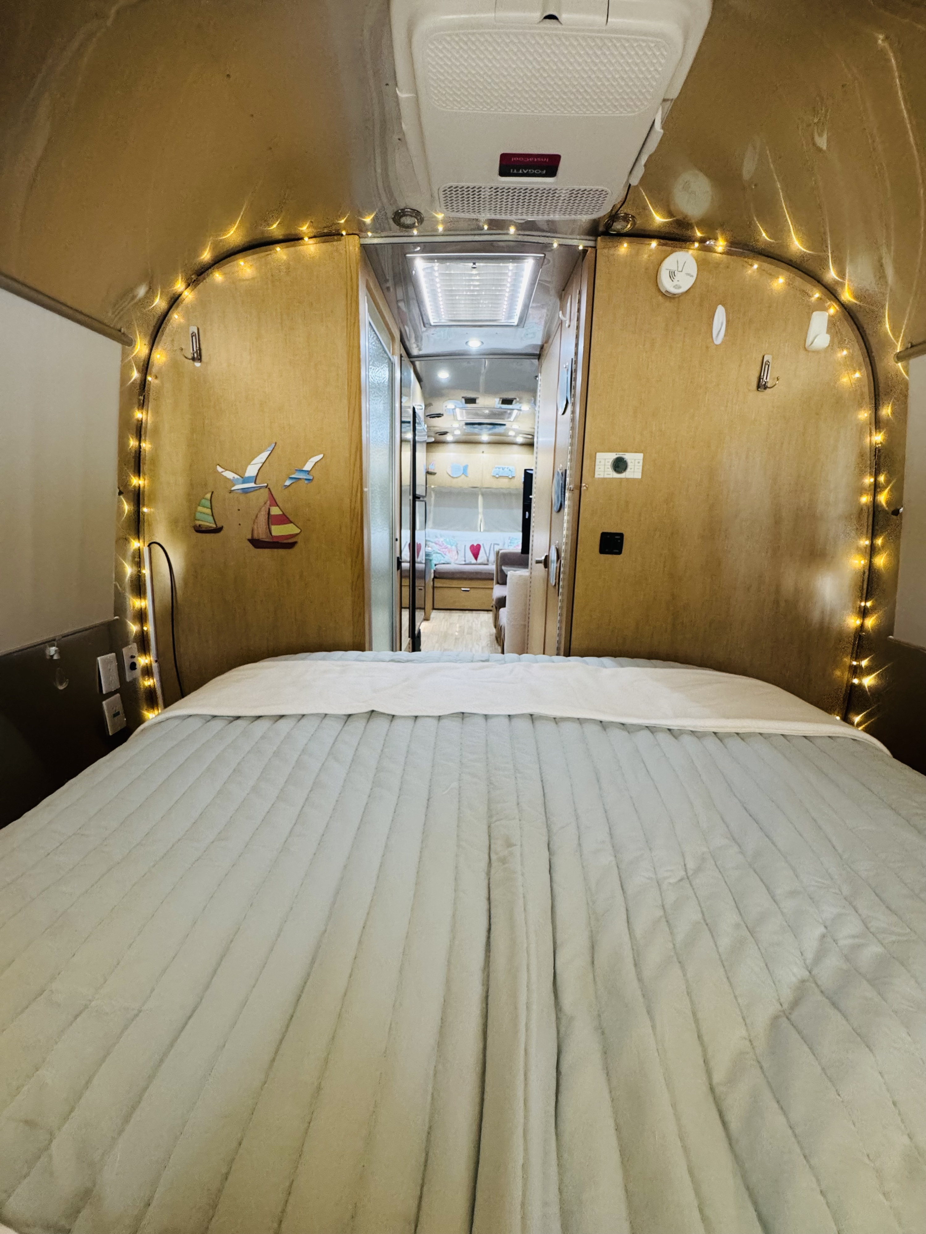 Cozy Airstream RV rental interior: bedroom with quilted blanket, string lights, and living area view.. Airstream Flying Cloud 2017