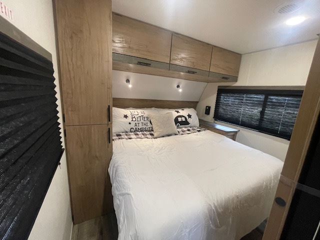 Cozy RV rental bedroom featuring a white bed, overhead cabinets, and a compact wardrobe. Ideal for road trips.. Forest River Campsite Reserve 26CJ 2025