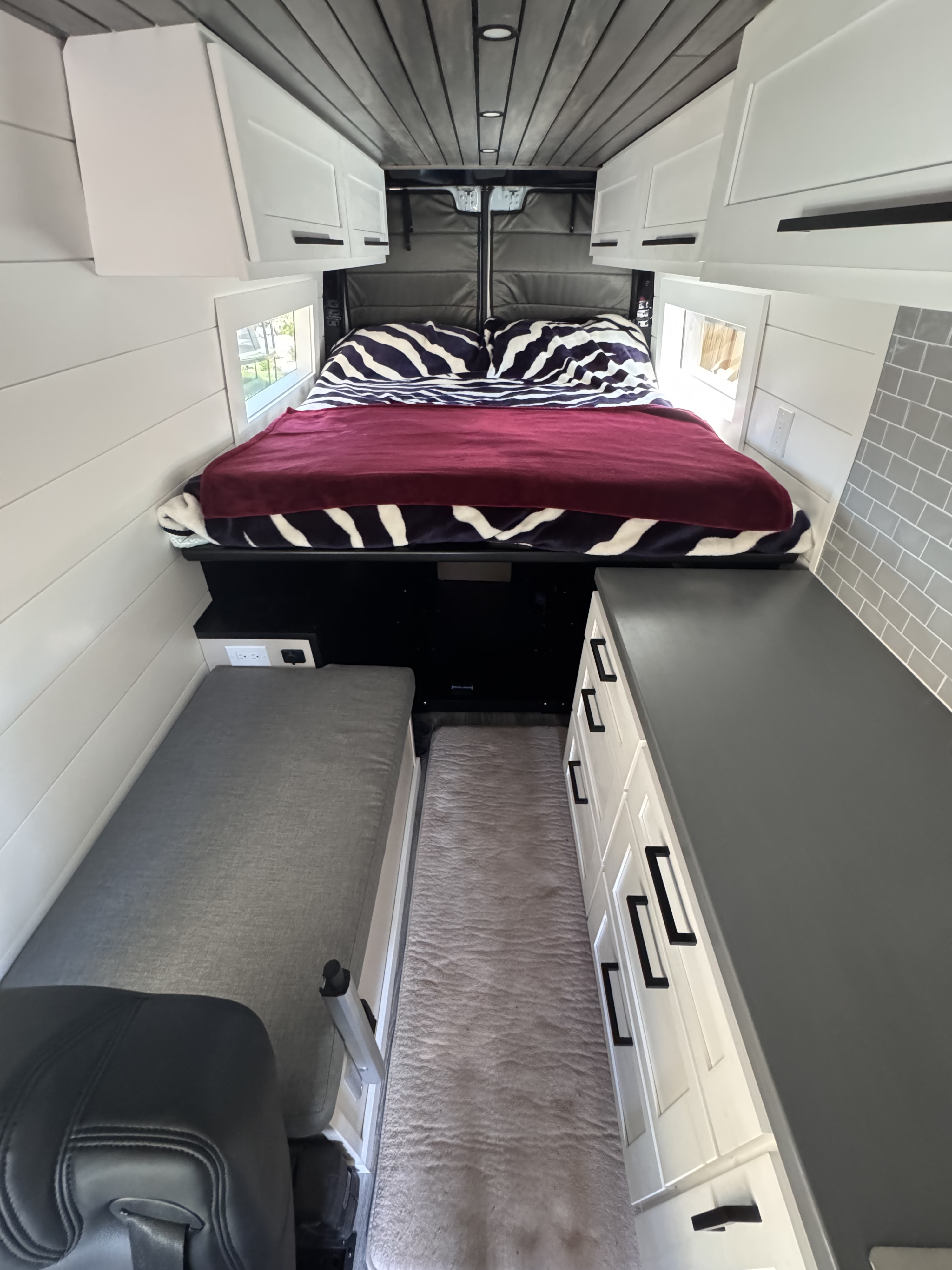 Modern rv rental interior: compact living with a cozy bed, white cabinets, and sleek gray accents.. Mercedes-Benz Sprinter 2012