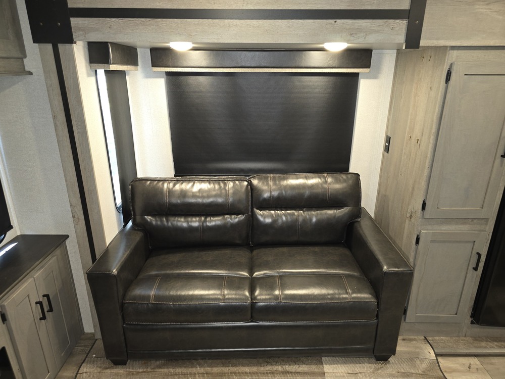 Cozy RV rental interior featuring a dark leather two-seater sofa and overhead lighting for a comfortable journey.. Keystone Outback 341RD 2021
