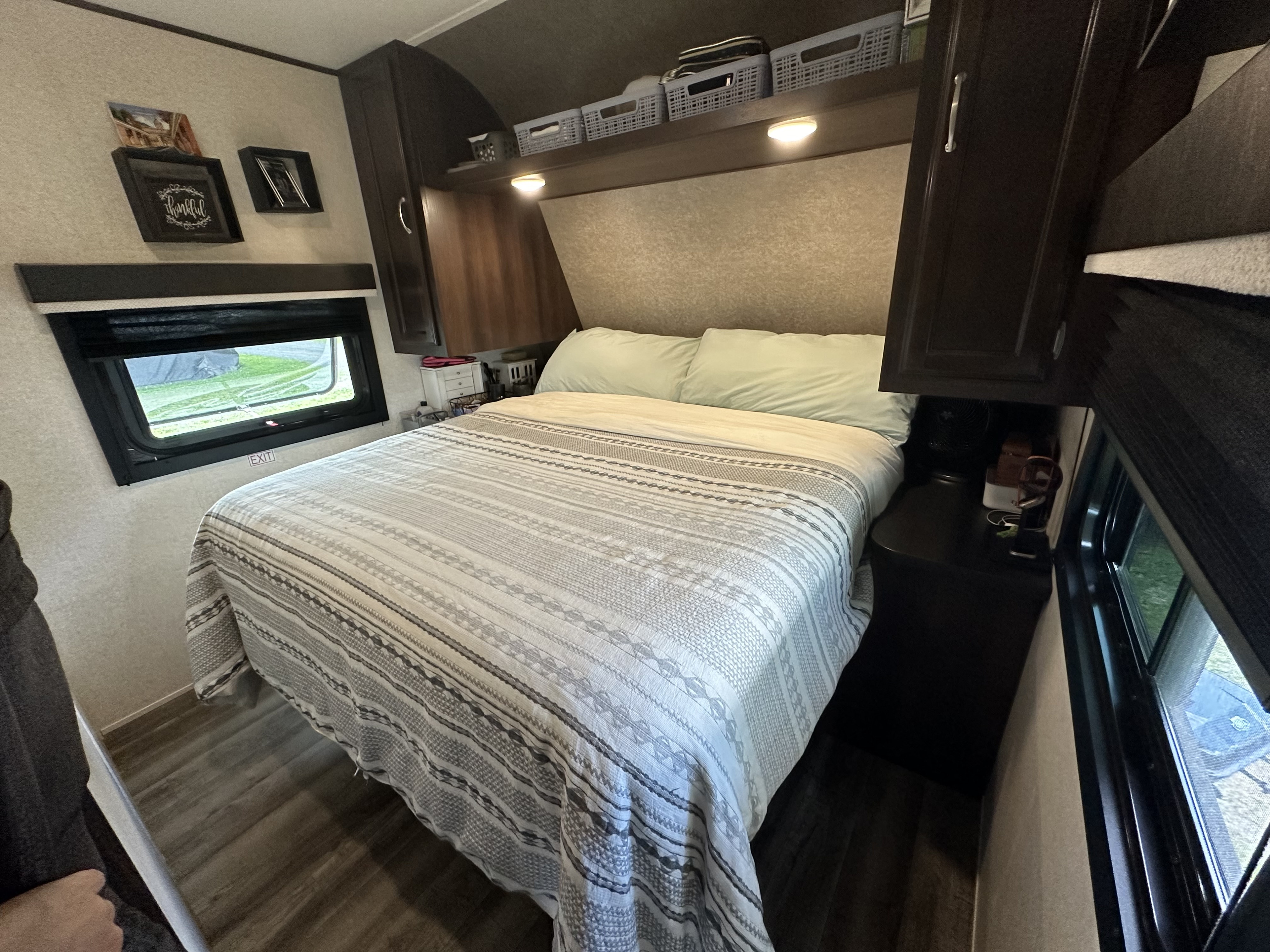 Interior of a comfortable RV rental bedroom, featuring a patterned bed, overhead storage, and a window.. Jayco Jay Flight 2018