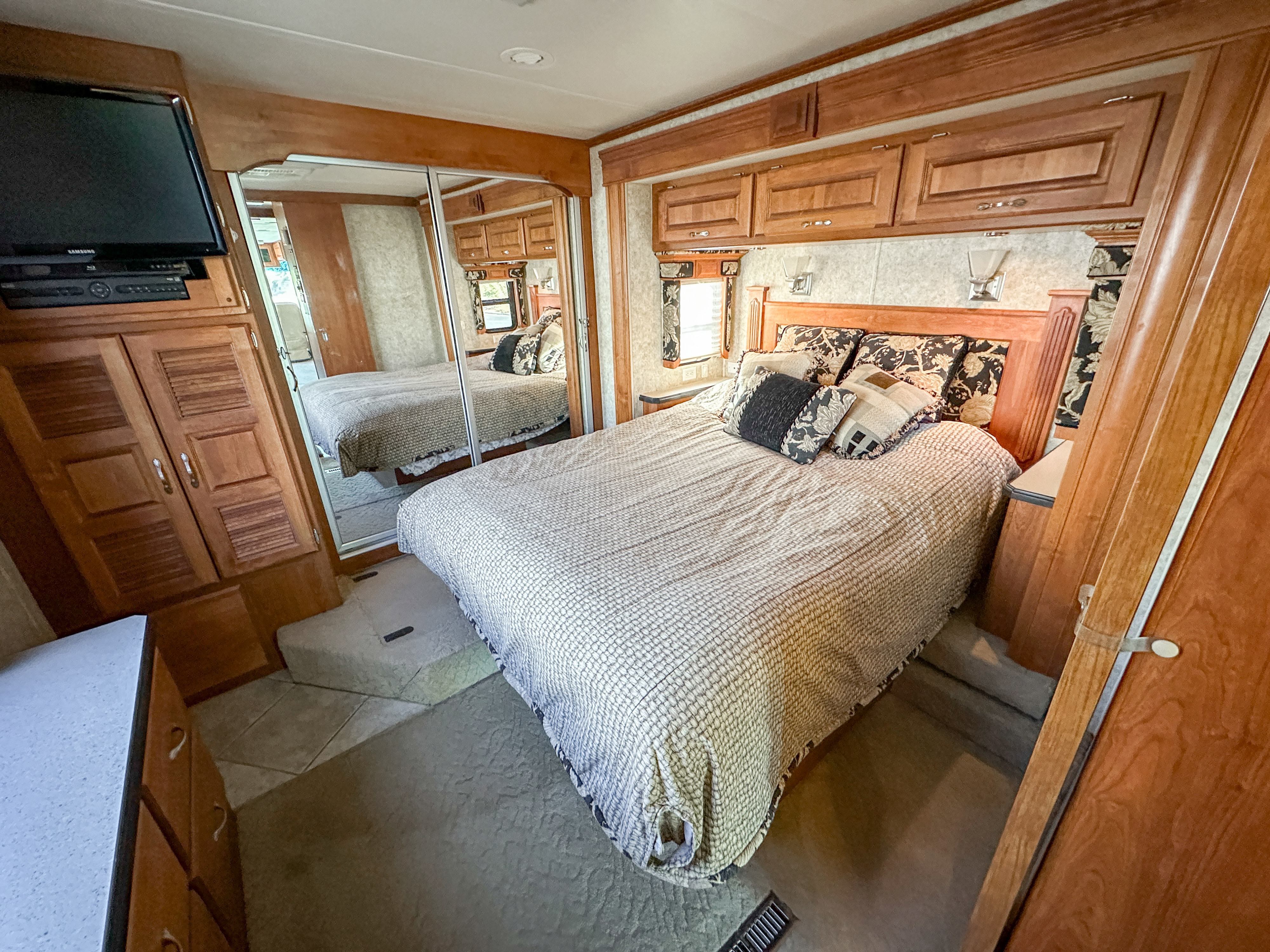 Spacious RV rental bedroom with a comfortable bed, mirrored closet, TV, and ample storage for your travels.. Holiday Rambler Endeavor 2006