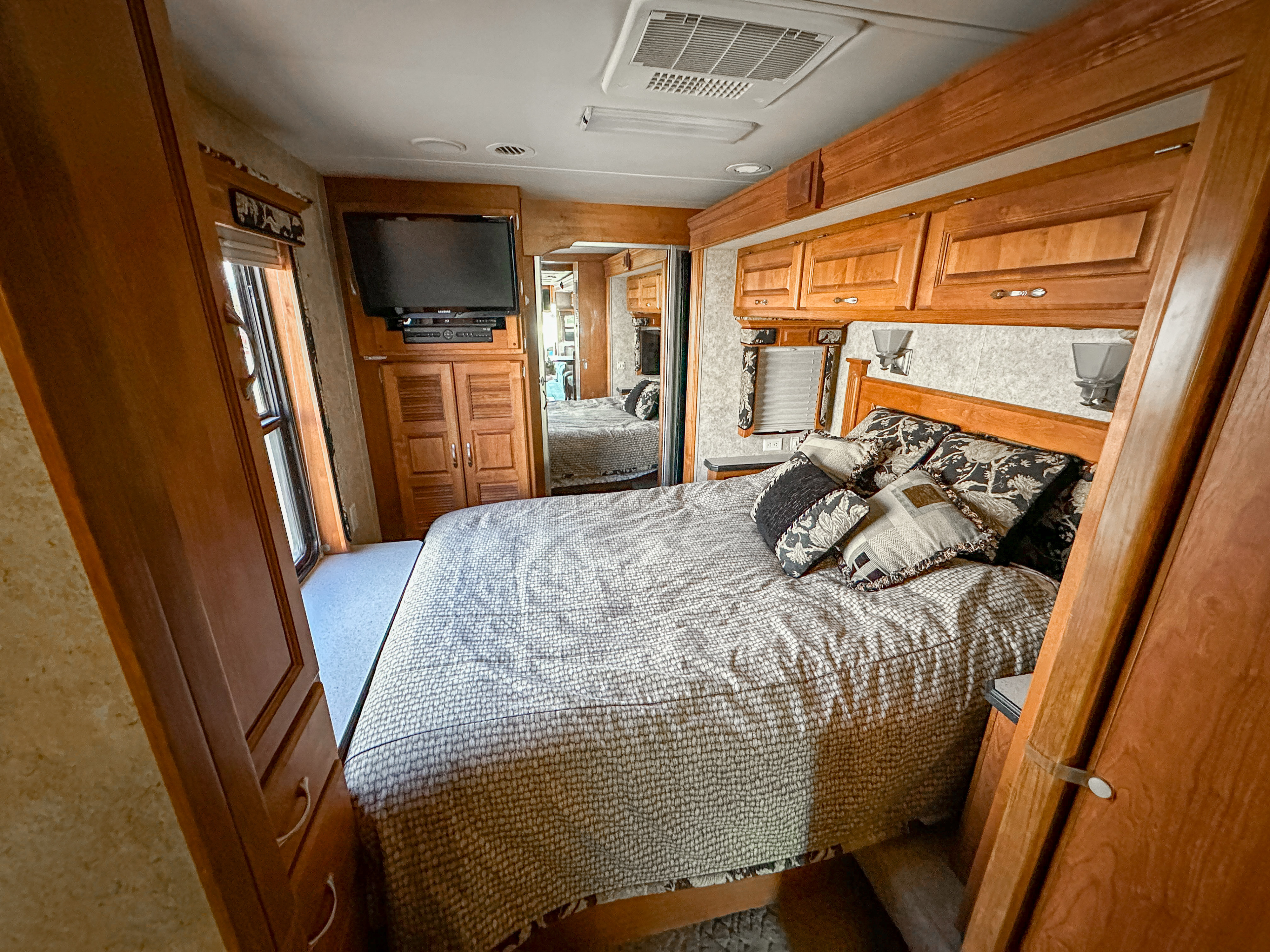 An RV rental bedroom featuring a cozy bed, wall-mounted TV, wood cabinetry, and a mirrored closet door.. Holiday Rambler Endeavor 2006