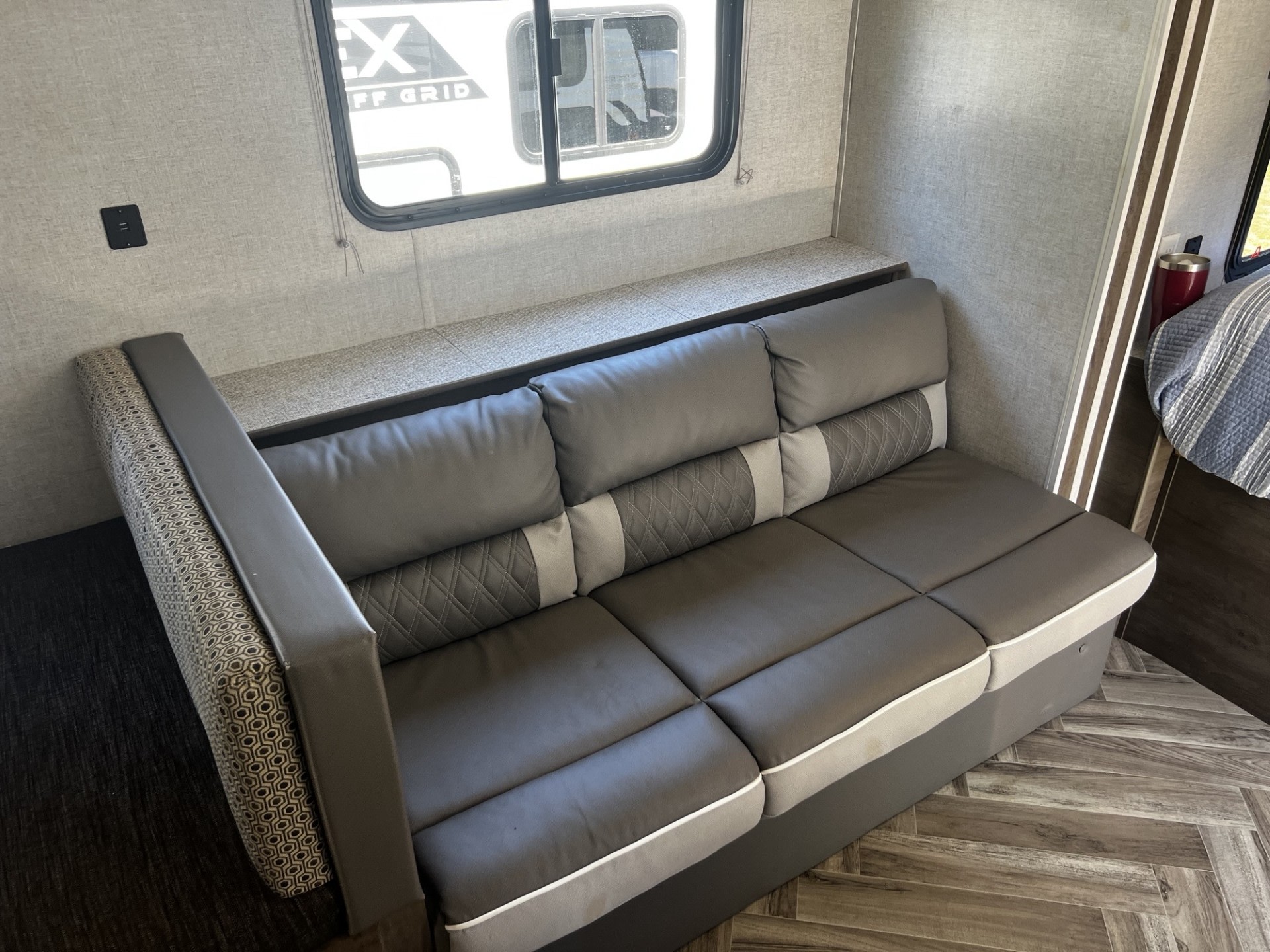 RV rental features: cozy gray sofa with accent pillows, built-in shelf, USB charging port, and window view.. Forest River Wildwood 2021