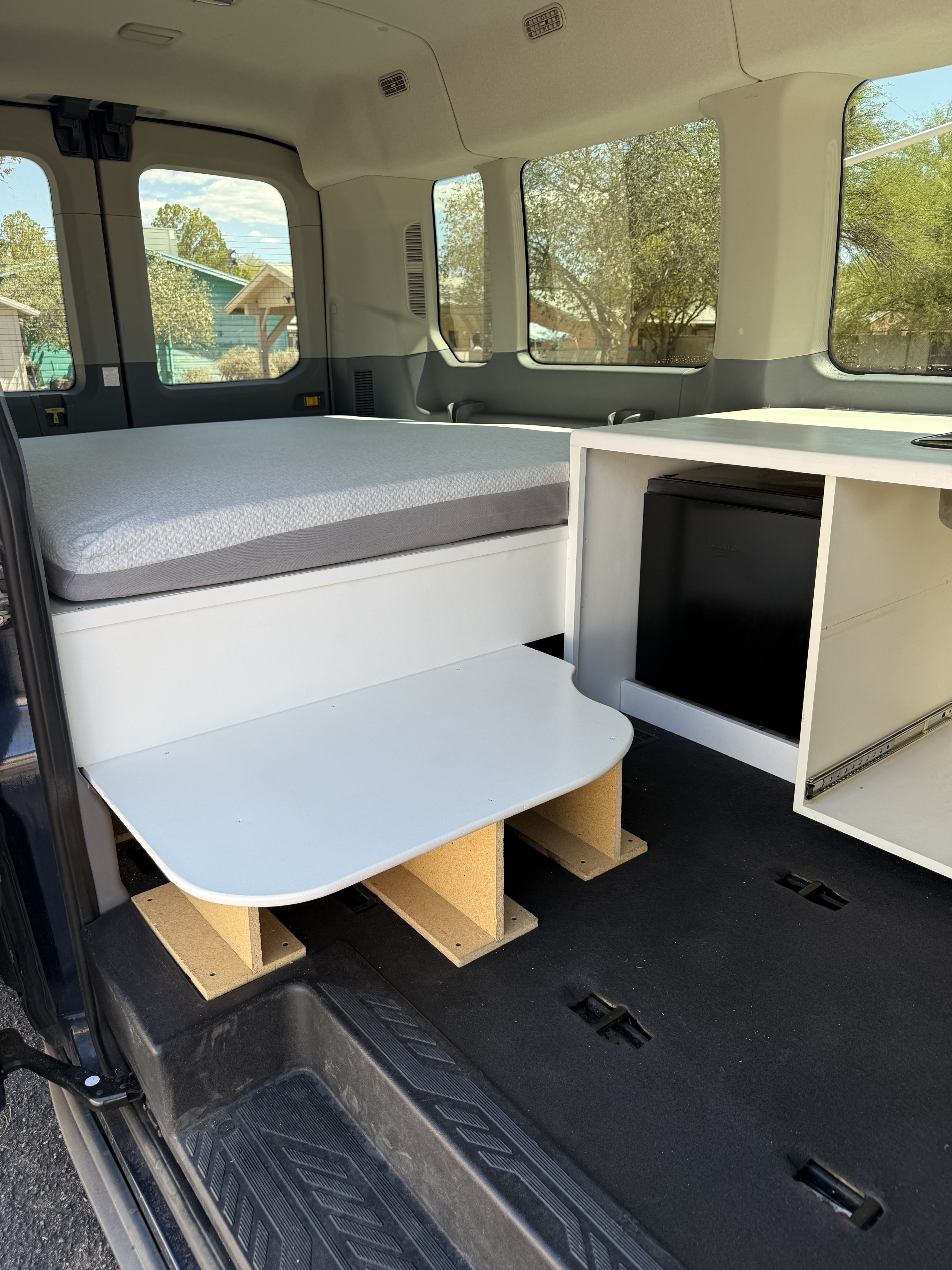 Interior of an RV rental camper van with a cozy bed, integrated storage, and mini-fridge for comfortable travel.. Ford Transit 3500 2015