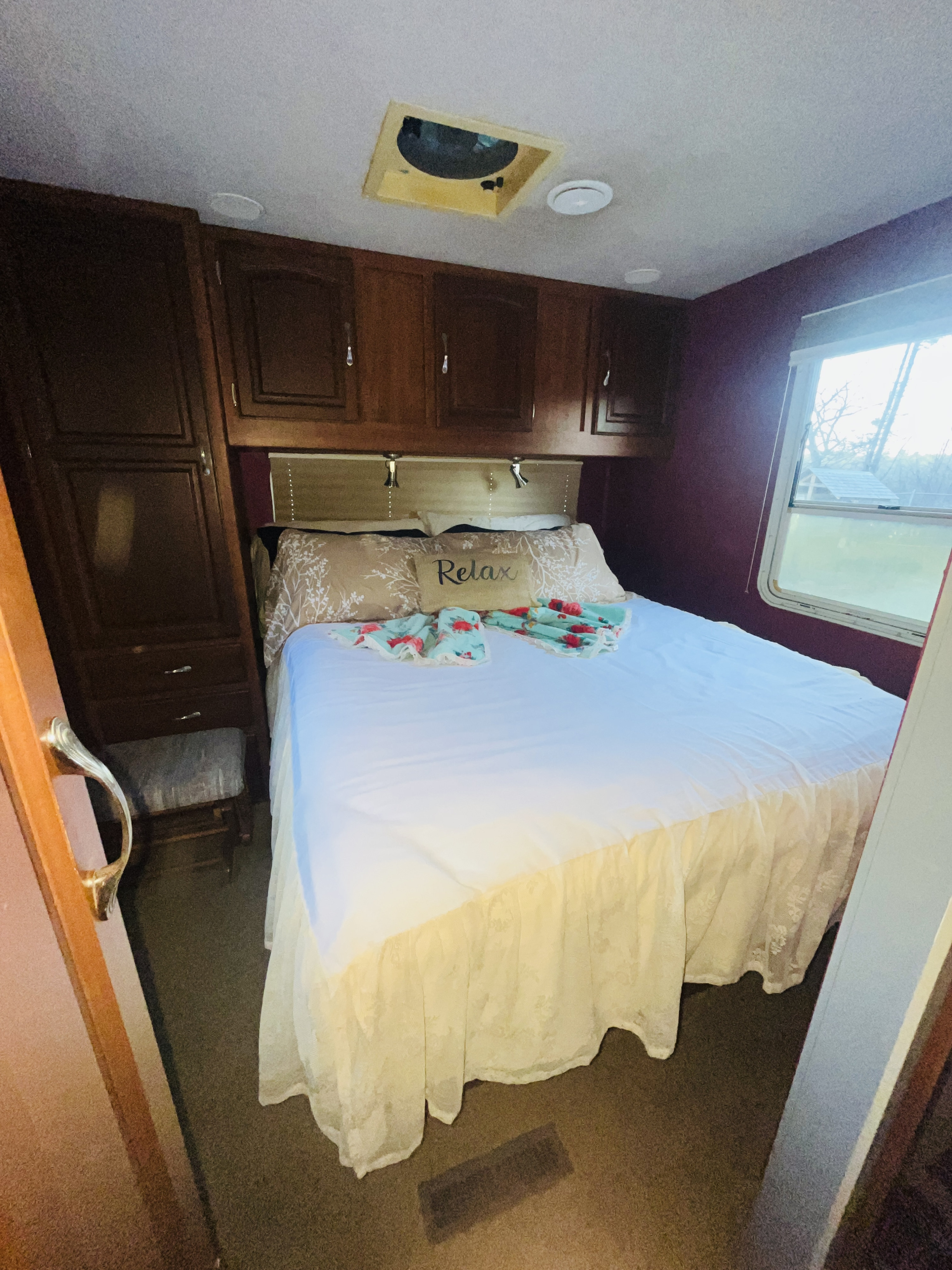 Cozy RV rental bedroom with a comfy bed, "Relax" pillow, wooden cabinets, and a window view, offering comfort on the road.. Jayco Granite Ridge 2006