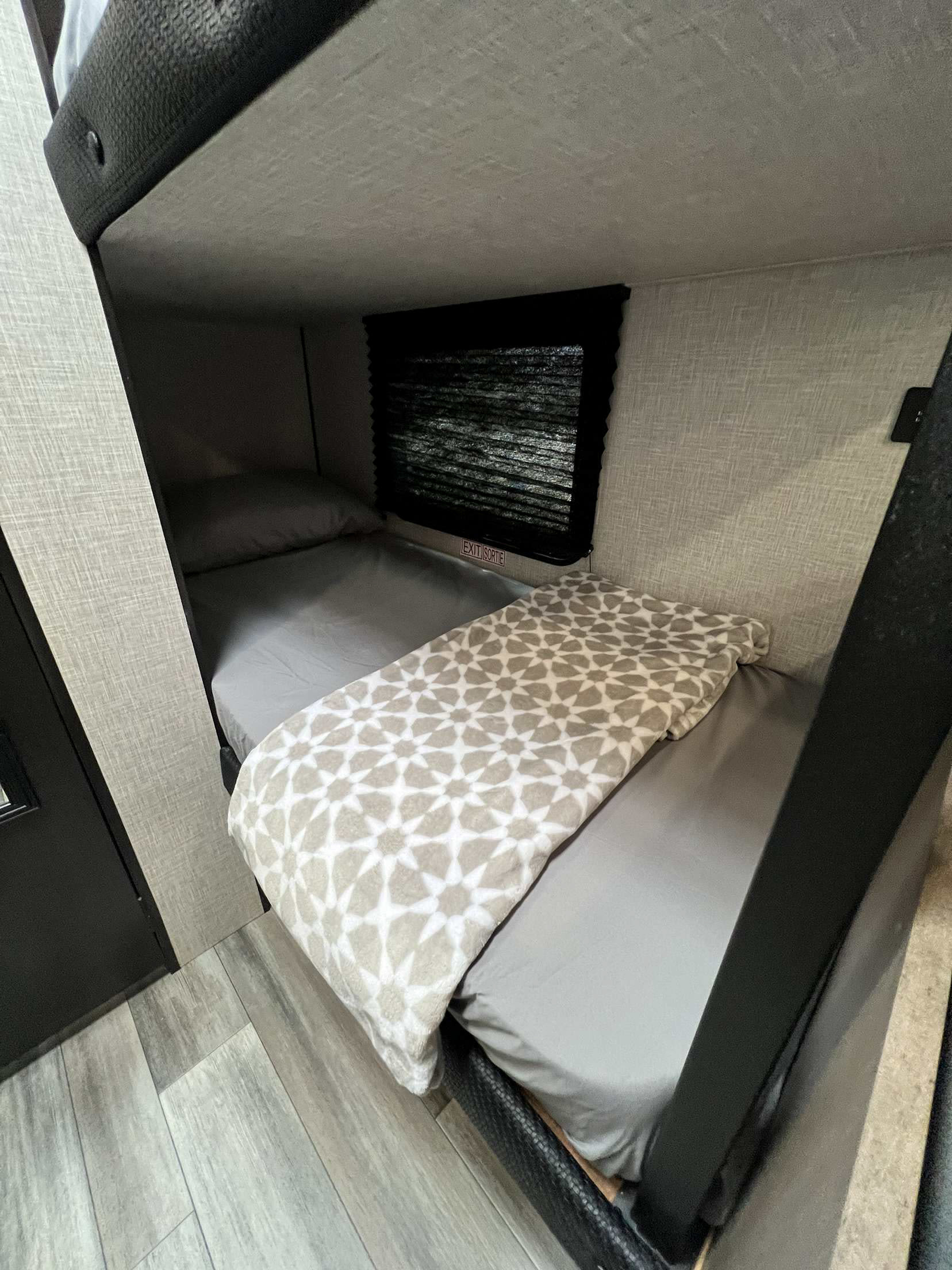 Cozy RV rental interior with bunk beds. Lower bunk has grey sheets & a patterned blanket. An exit window is visible.. Jayco Jay Flight SLX 170BHW 2025