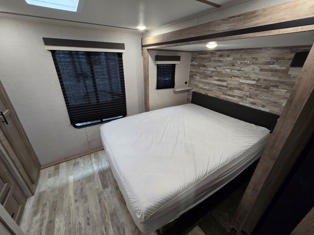 Spacious RV rental bedroom featuring a large bed, window with blinds, and modern wood accents.. Gulf Stream Kingsport 33DBDB 2024