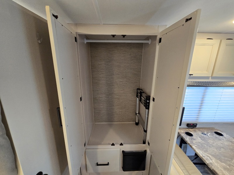 Open RV rental wardrobe with hanging rod and compact ladder, showcasing smart interior storage.. Thor Four Winds 22E 2023