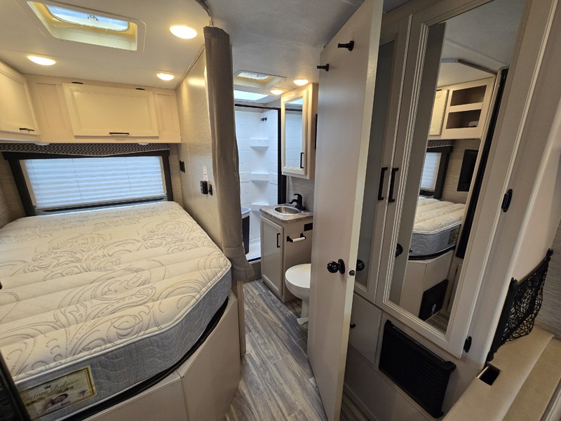 RV rental: Bedroom with a cozy bed and overhead storage, plus a compact bathroom with toilet, sink, and shower.. Thor Four Winds 22E 2023