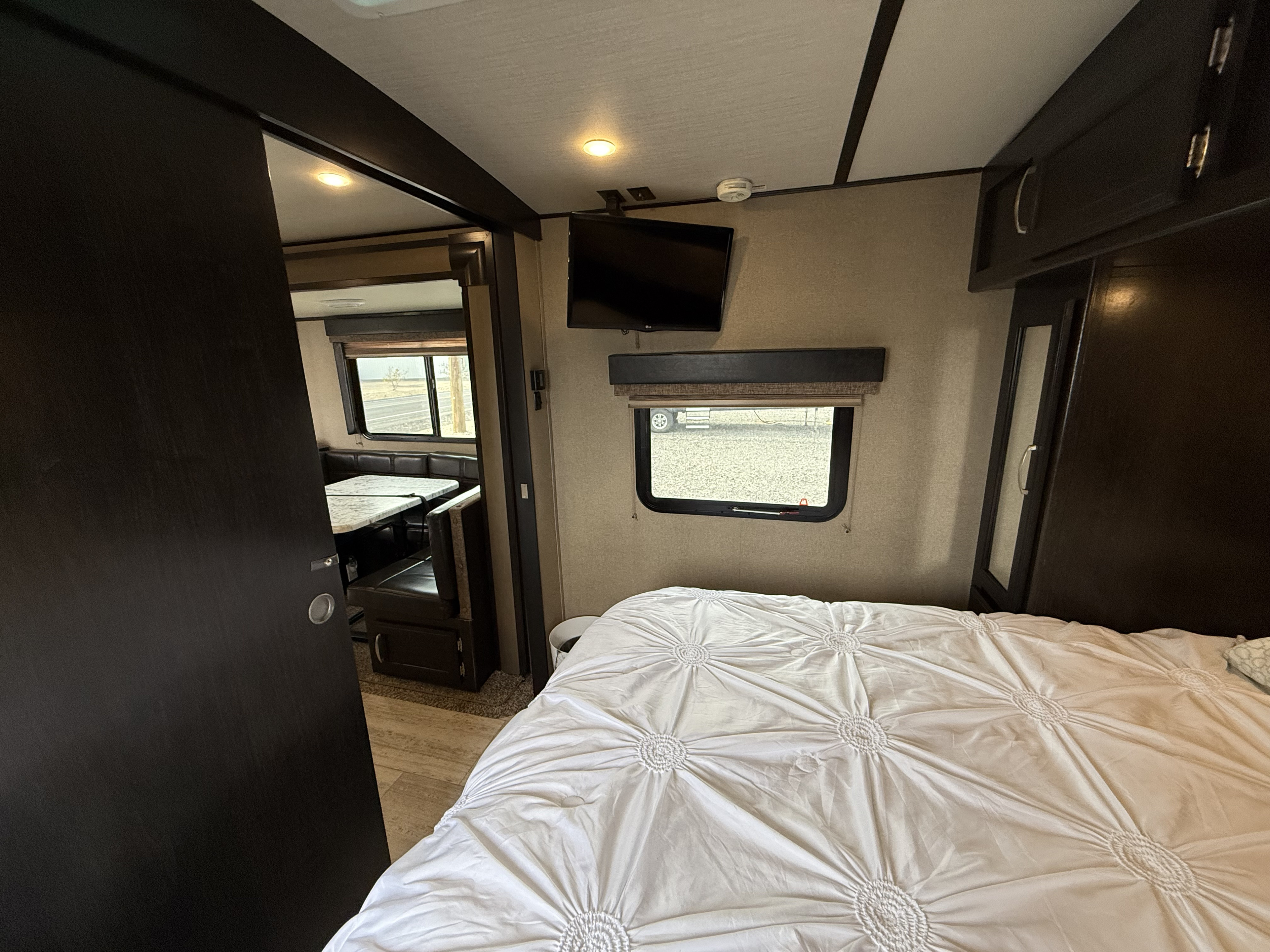 RV rental interior: cozy bedroom with a white comforter, TV, and an adjacent dining area with booth seating.. Grand Design Imagine 2018