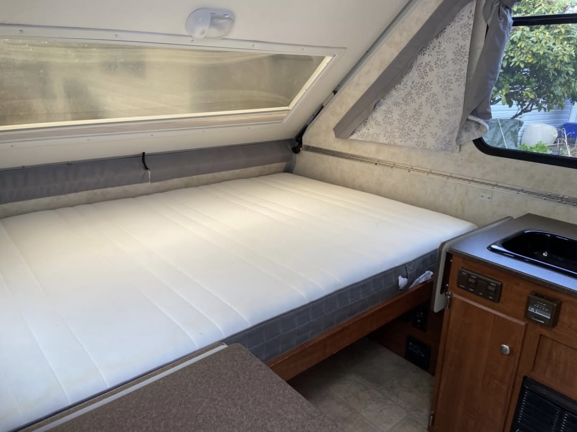 Spacious RV rental interior featuring a comfortable bed, large window, and compact kitchenette.. A liner Classic 2013