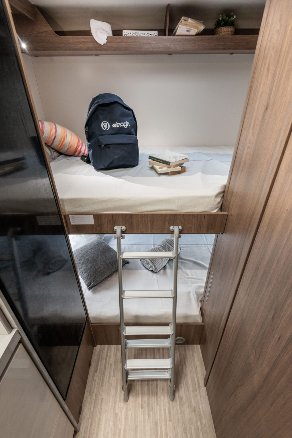 RV rental interior features cozy bunk beds with a ladder. A backpack & books are on the top bunk, a pillow on the bottom.. Elnagh baron 20 2025