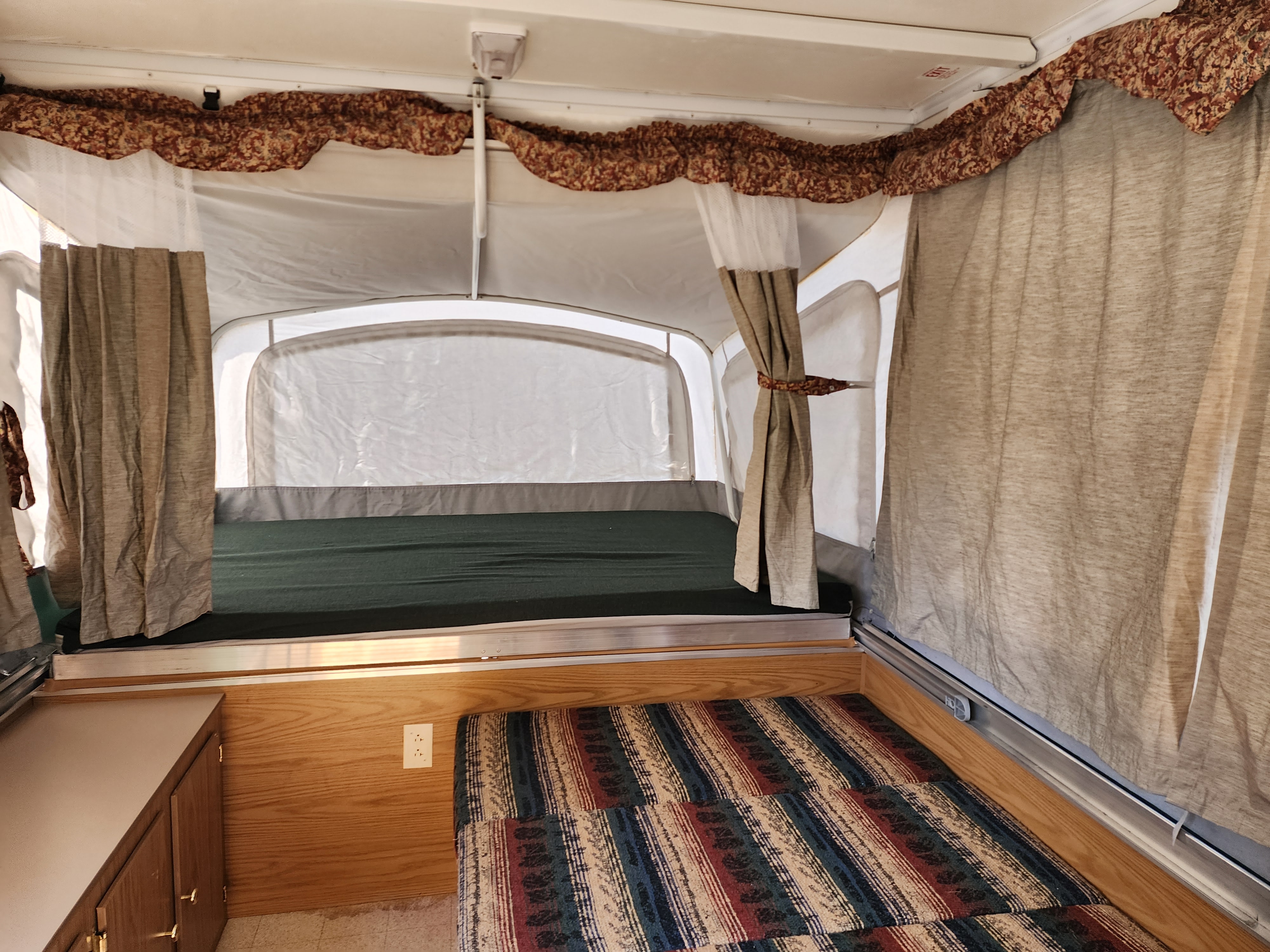 Spacious RV rental pop-up camper interior. Two distinct bed areas with ample curtains and storage are visible.. Coleman Sedona 1999