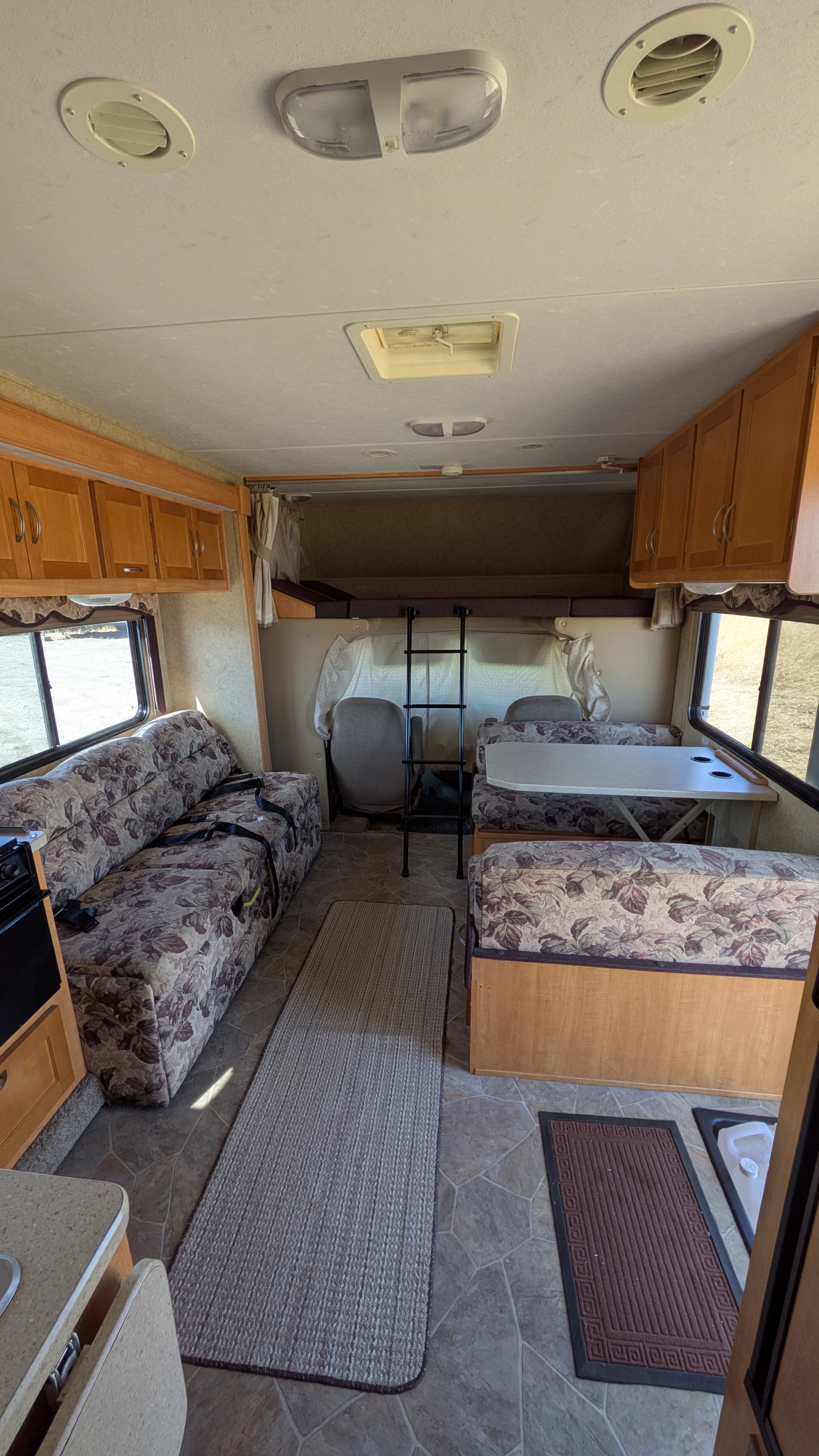 Spacious RV rental interior featuring a cozy dinette, patterned sofa, and overhead bunk.. Forest River Sunseeker 2010