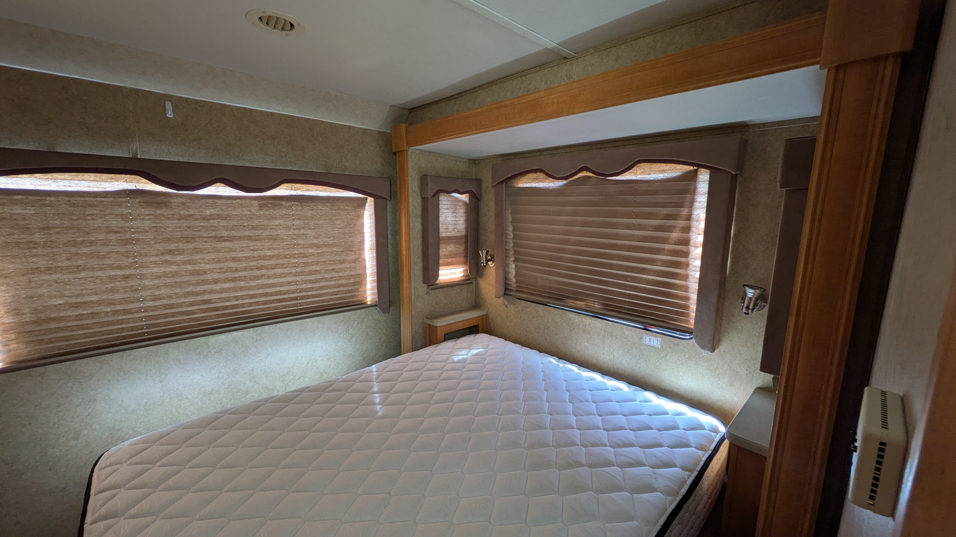 Spacious RV rental bedroom with a comfortable bed, multiple windows featuring pleated blinds, and built-in RV fixtures.. Forest River Sunseeker 2010