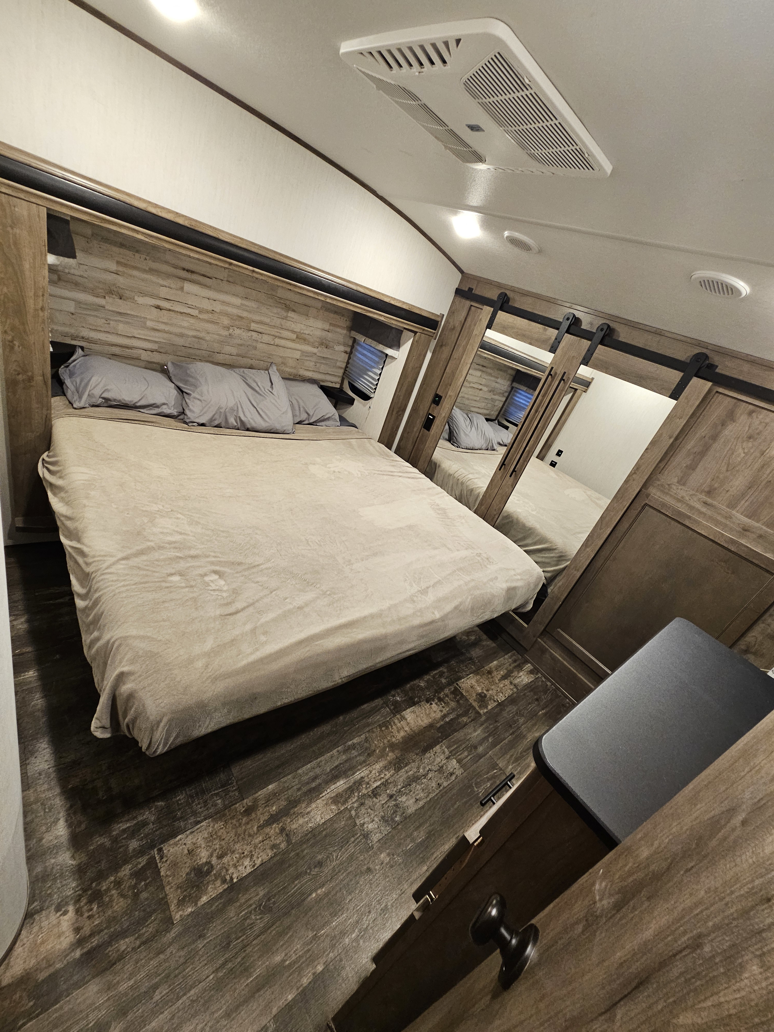 Comfortable RV rental bedroom with a spacious bed, wood-paneled accents, mirrored closet doors, and ceiling AC.. Forest River Sabre 2022