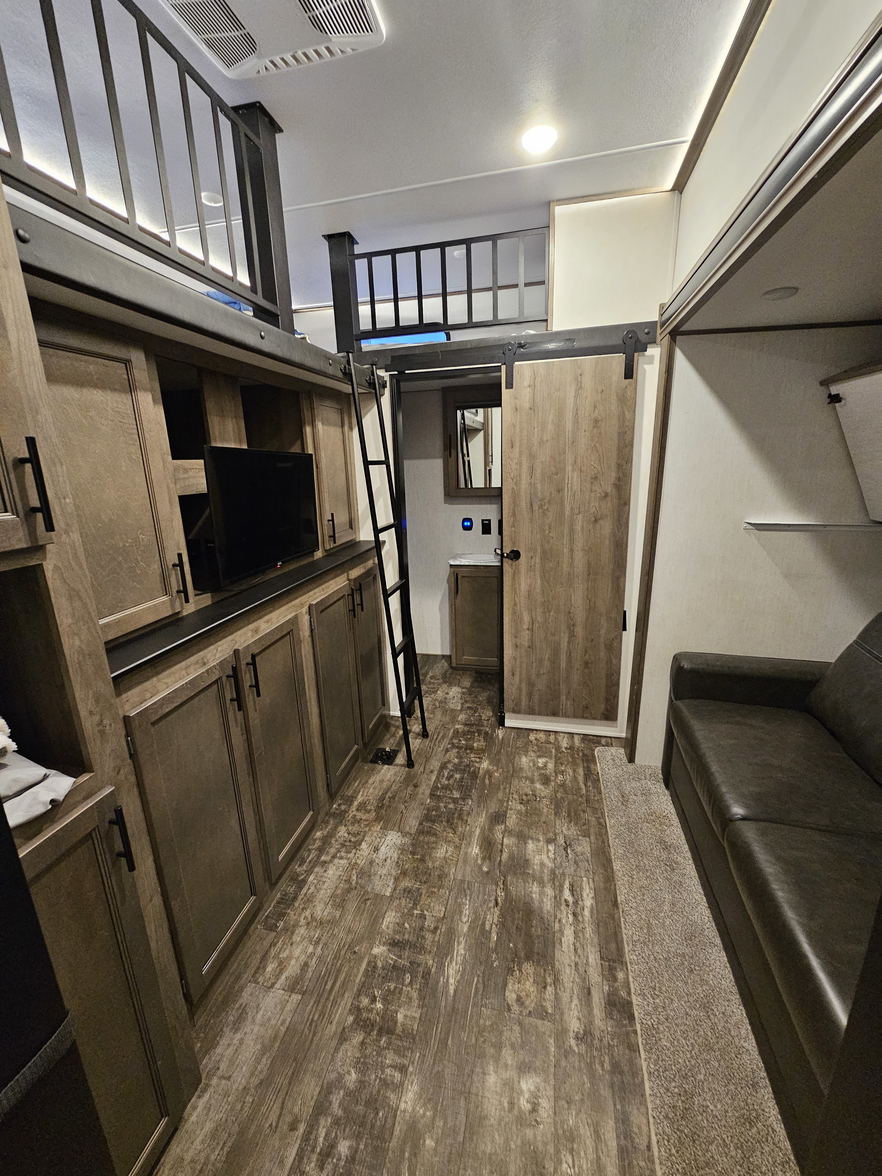 Cozy rv rental interior featuring a wooden floor, entertainment center, loft, and a barn door to the bathroom.. Forest River Sabre 2022