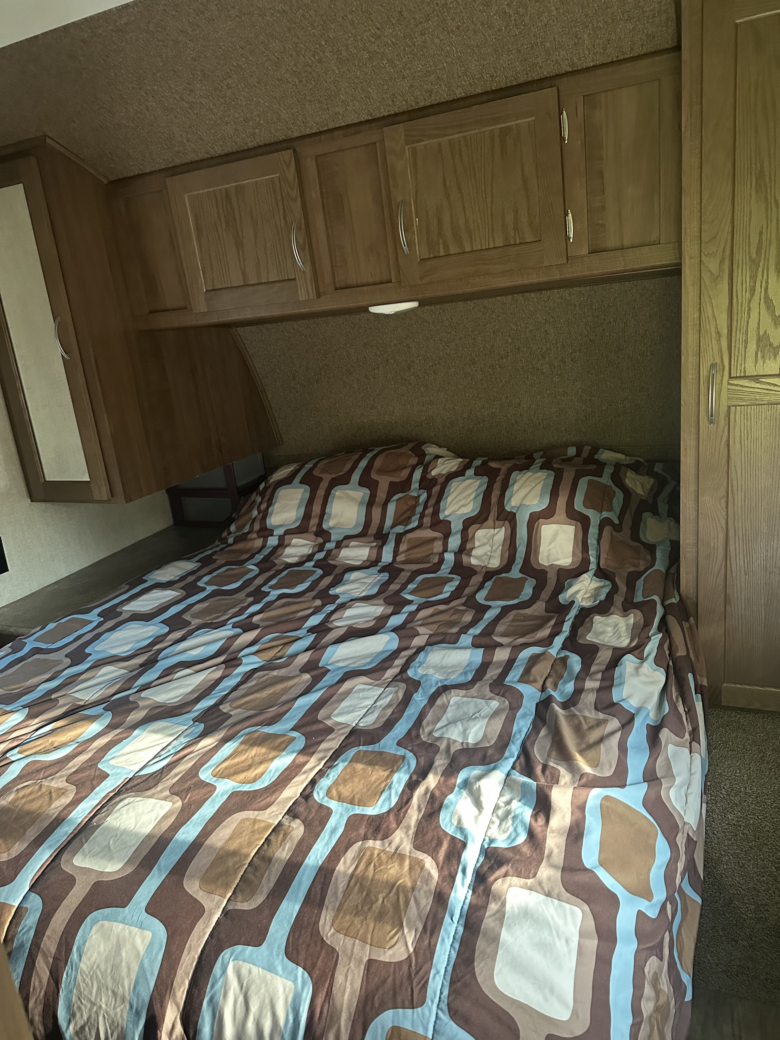 Cozy RV rental bedroom with geometric patterned bed, wood cabinets, and wardrobe for a relaxing getaway.. Gulf Stream Conquest 2017