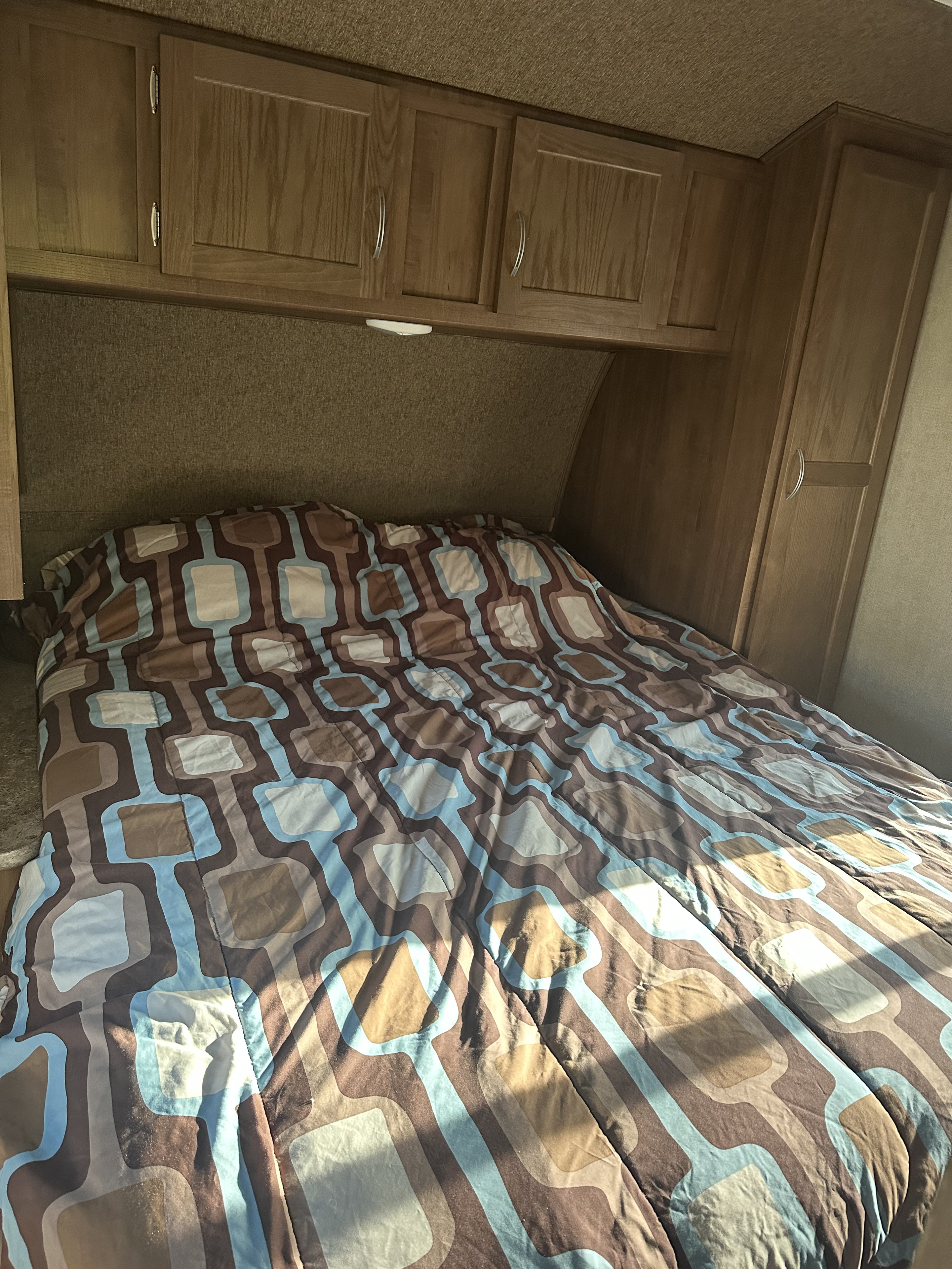 Cozy RV rental bedroom featuring a patterned comforter, overhead wood cabinets, and built-in wardrobe. Ideal for travel.. Gulf Stream Conquest 2017