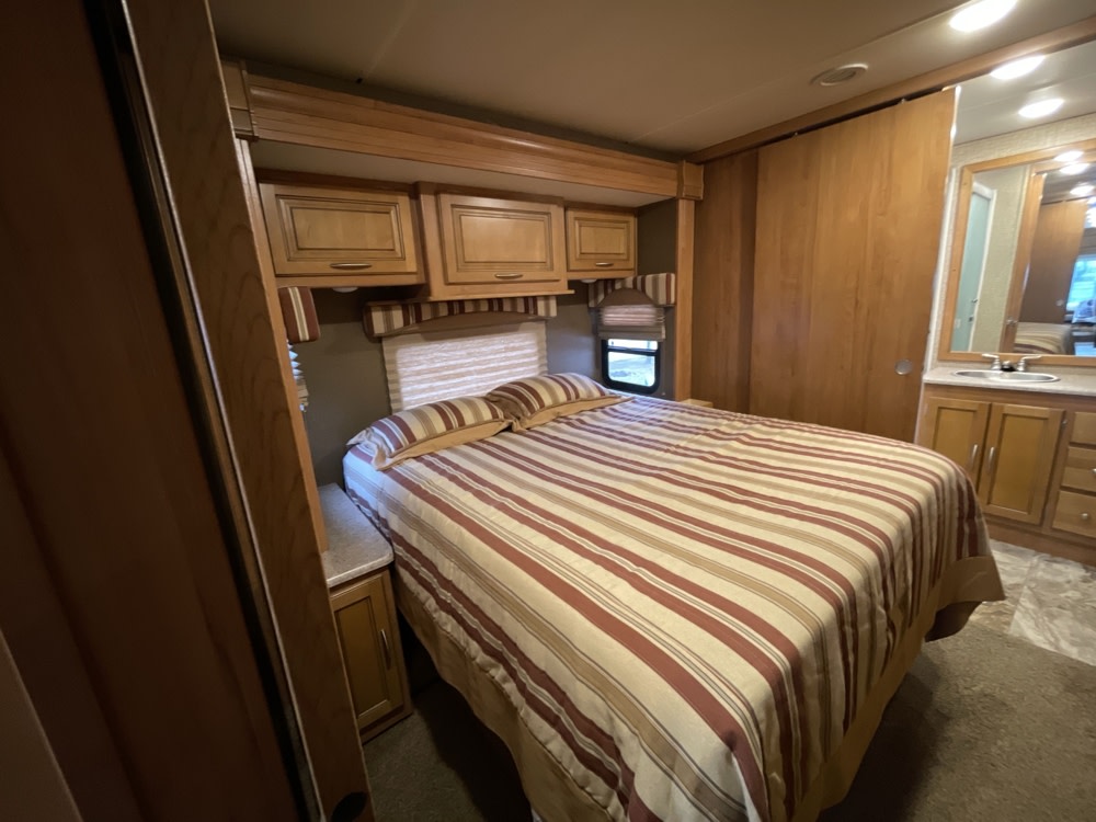 RV rental bedroom with striped bed, wooden cabinets, and an adjacent bathroom vanity.. Coachmen Mirada 2016
