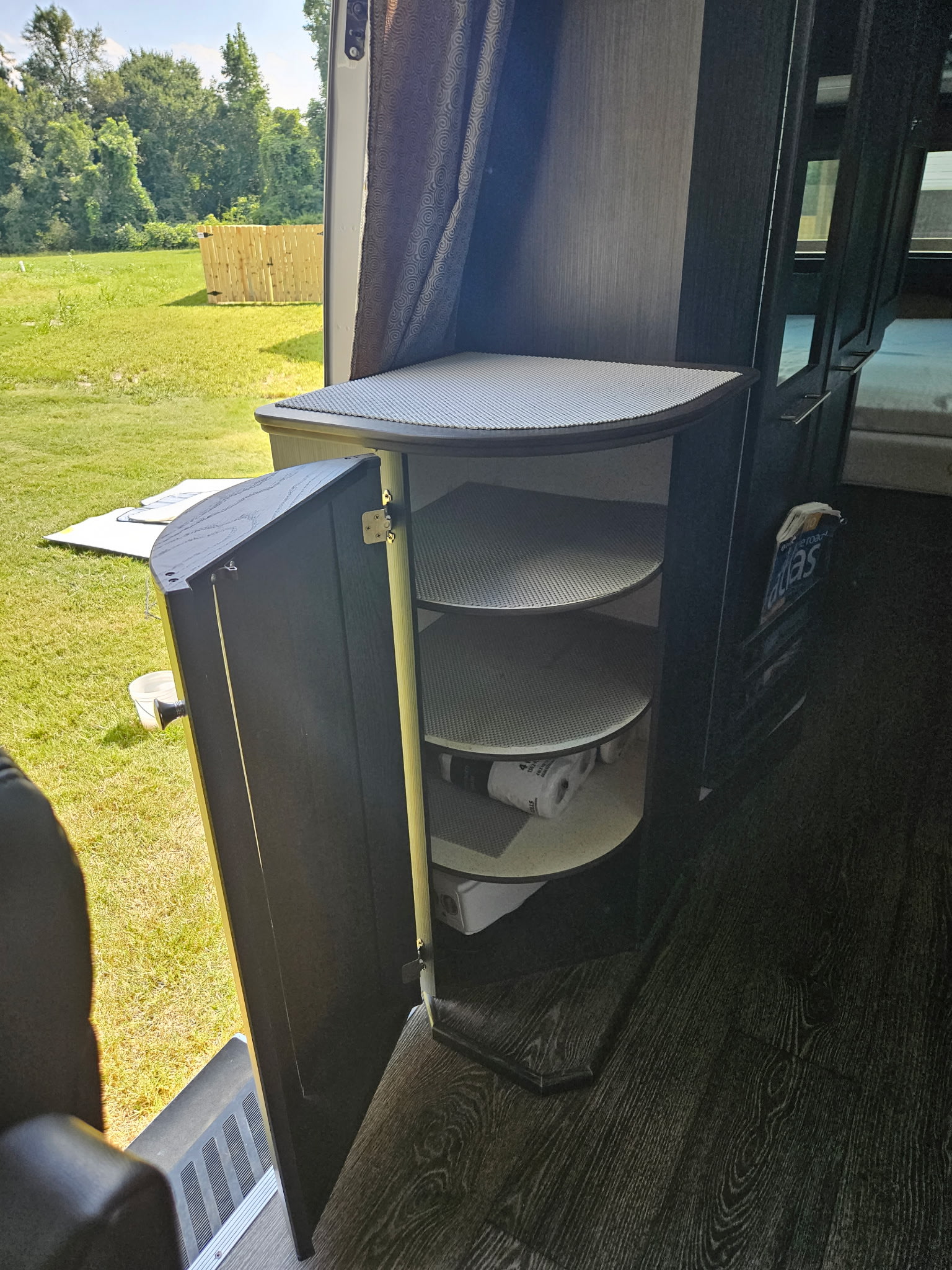 RV rental interior featuring an open dark cabinet with three round shelves, providing organized storage and a view of green outdoors.. Roadtrek Mercedes Sprinter Adventurous Rs 2018