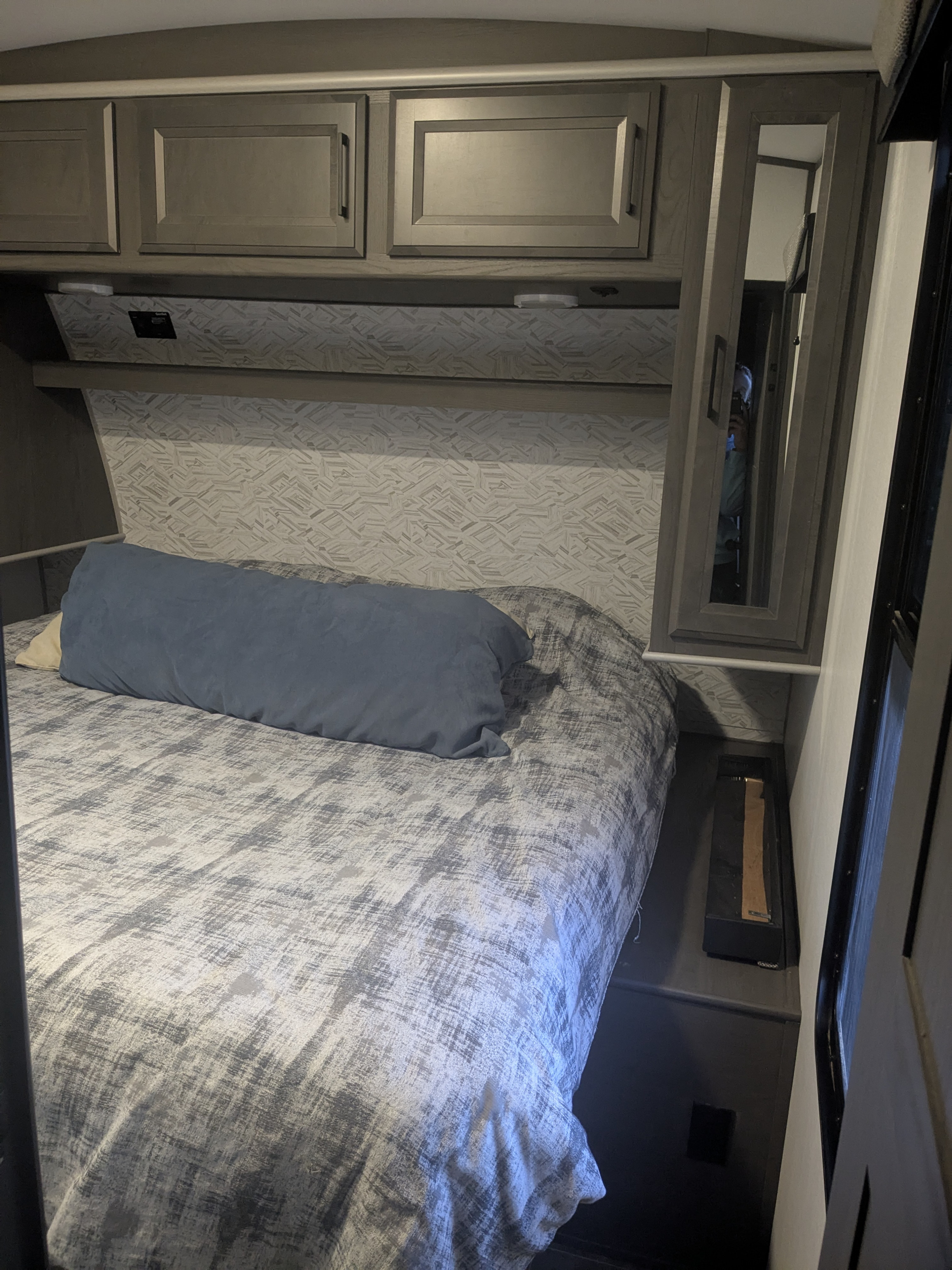 RV rental bedroom featuring a comfy bed with blue pillow, gray overhead cabinets, and patterned walls.. Cruiser Rv Corp Stryker 2022