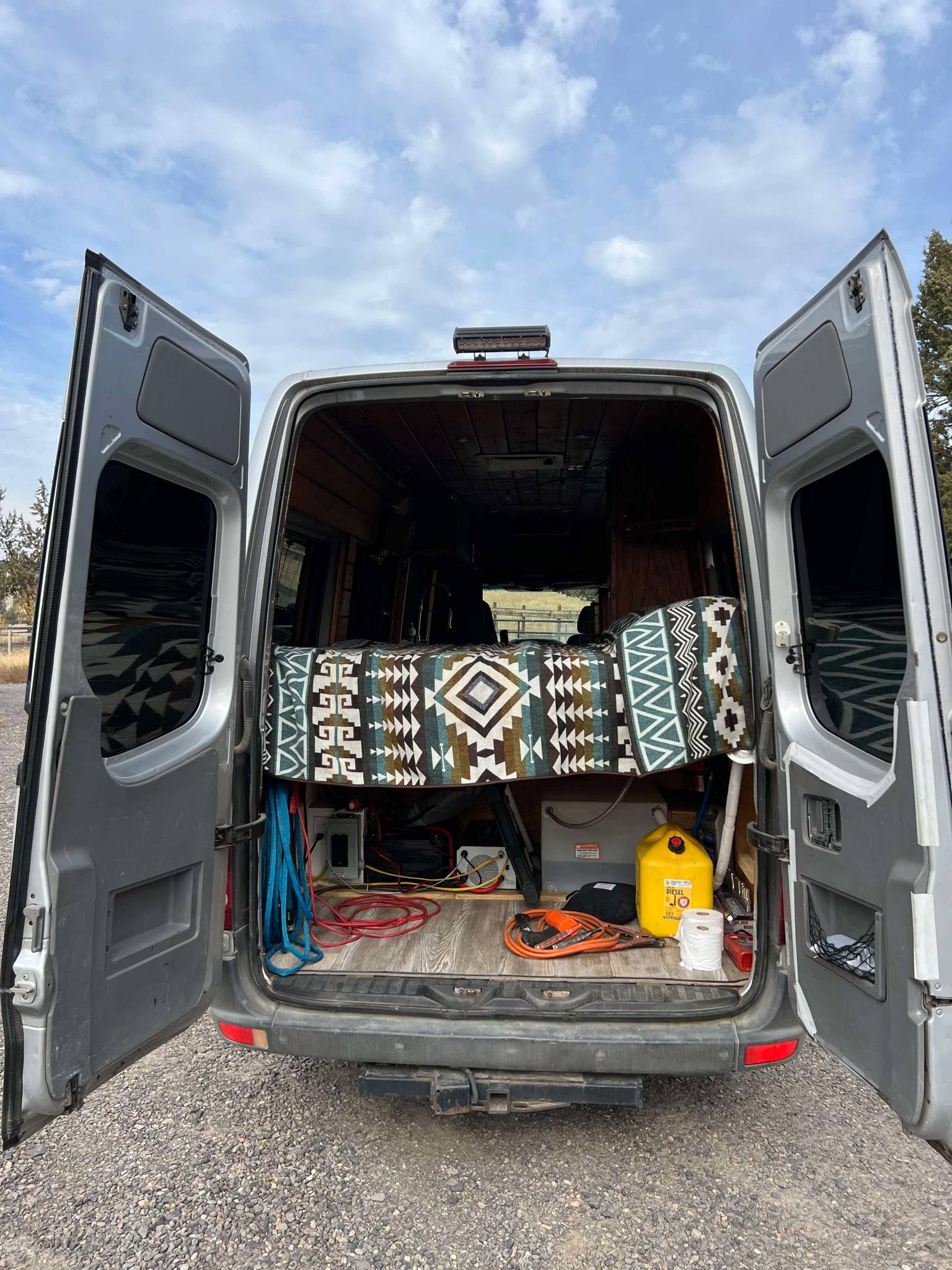 This RV rental camper van conversion reveals a patterned bed, utilities, & storage in its open rear, ready for adventure.. Mercedes Sprinter 2008