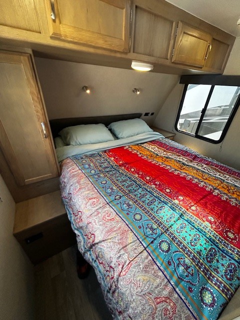 Cozy RV rental bedroom with a colorful bed, overhead cabinets, and window. Perfect for your next adventure.. Winnebago Minnie 2455BHS 2020