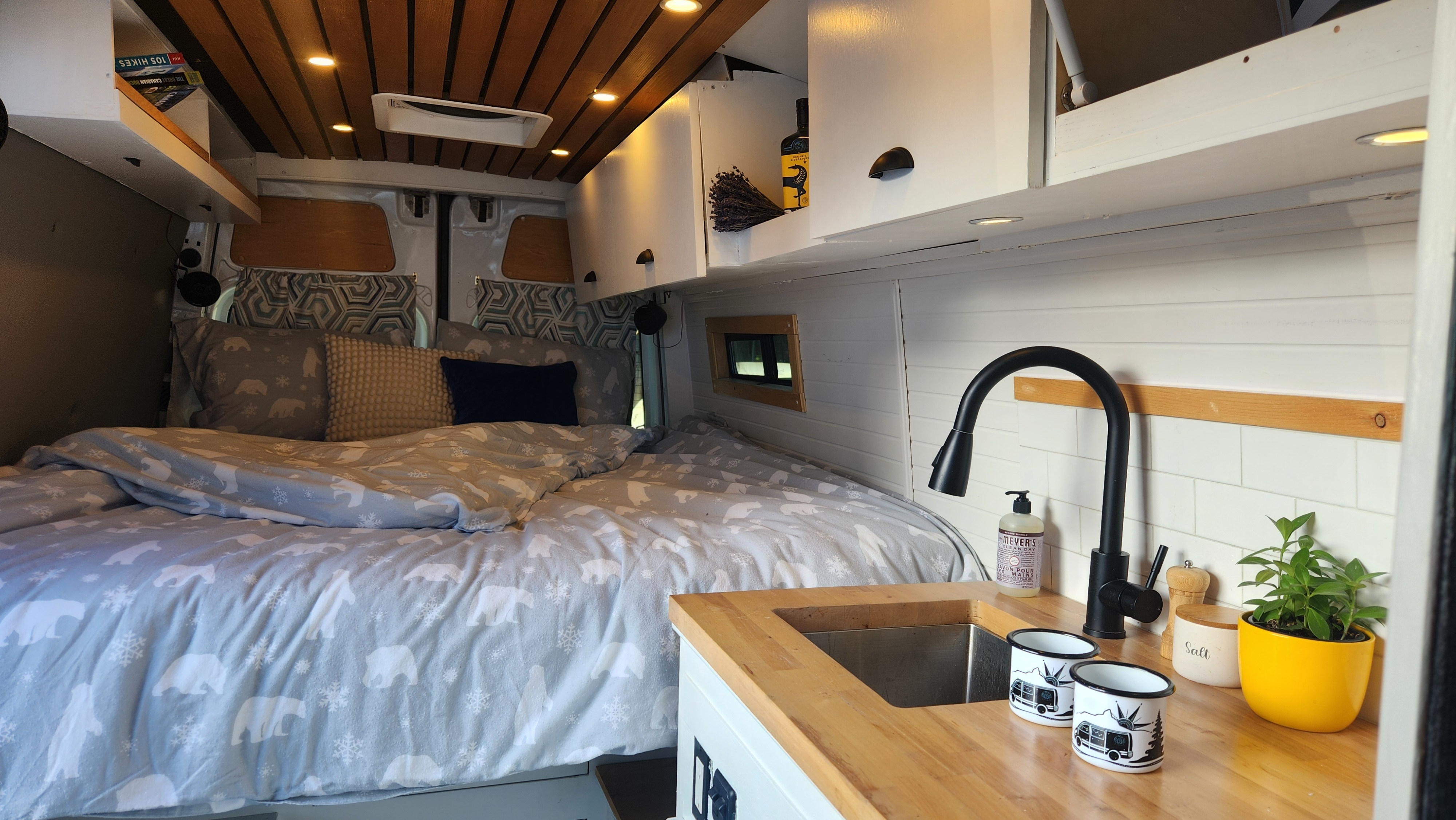 Interior of a bright RV rental: features a made bed with themed duvet, compact kitchen, and slatted wood ceiling.. Mercedes-Benz Sprinter 2011