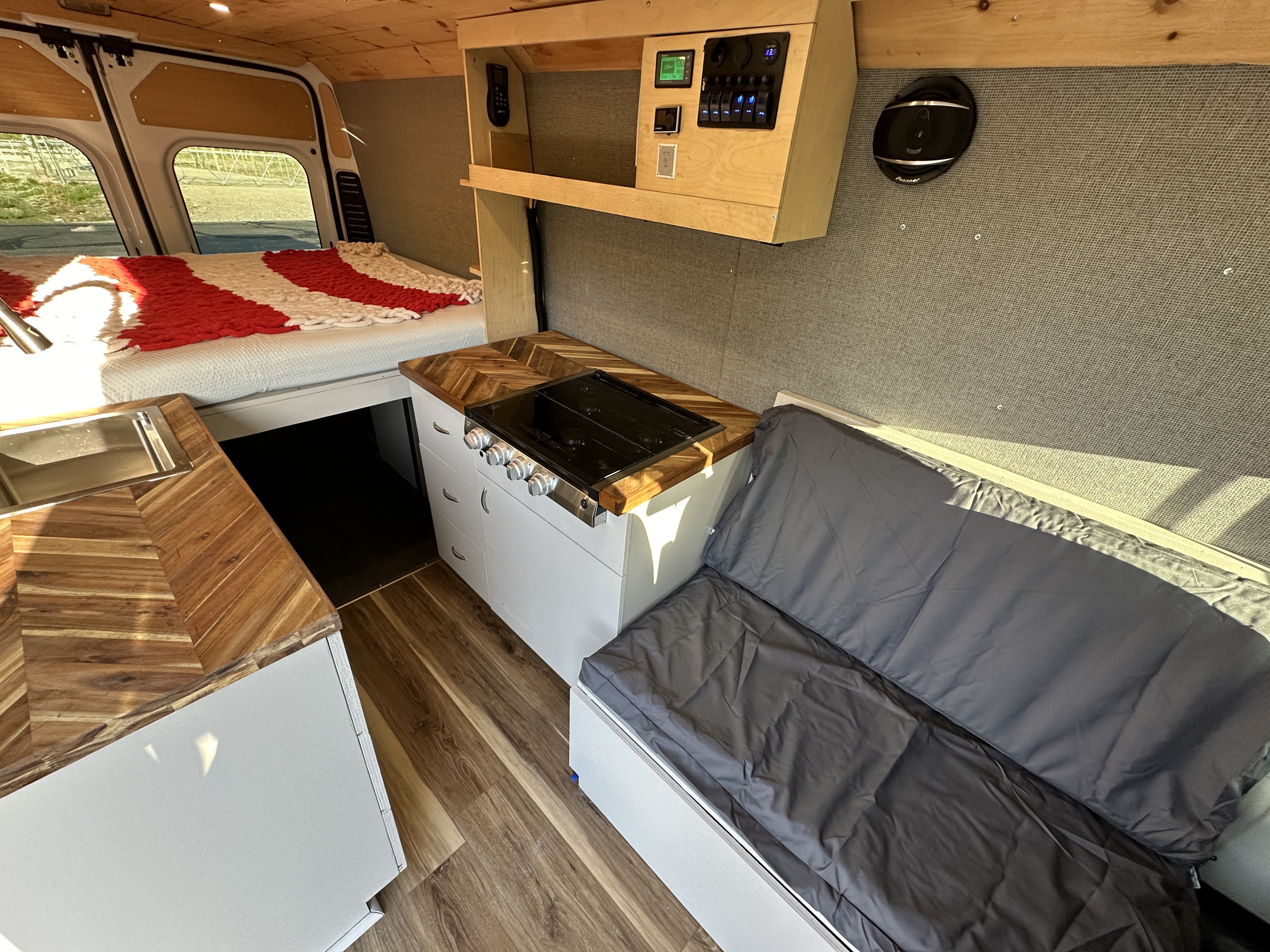Interior of an RV rental showing a bed, kitchenette with wood counters and stove, plus bench seating. Perfect for travel.. Dodge Promaster 3500 2020