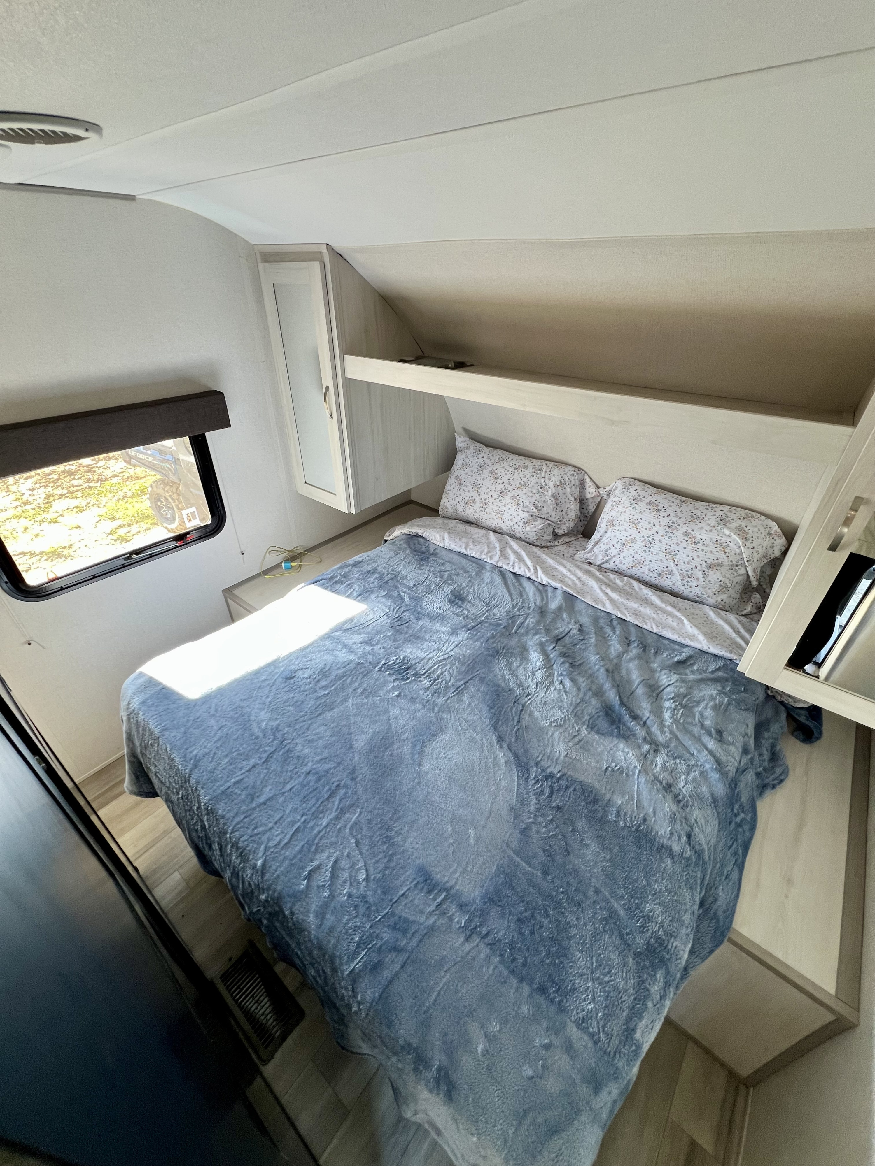 Step into comfort: an inviting RV rental bedroom with bed, bright window, overhead storage, and light-colored interior.. Prime Time RV Tracer 2022