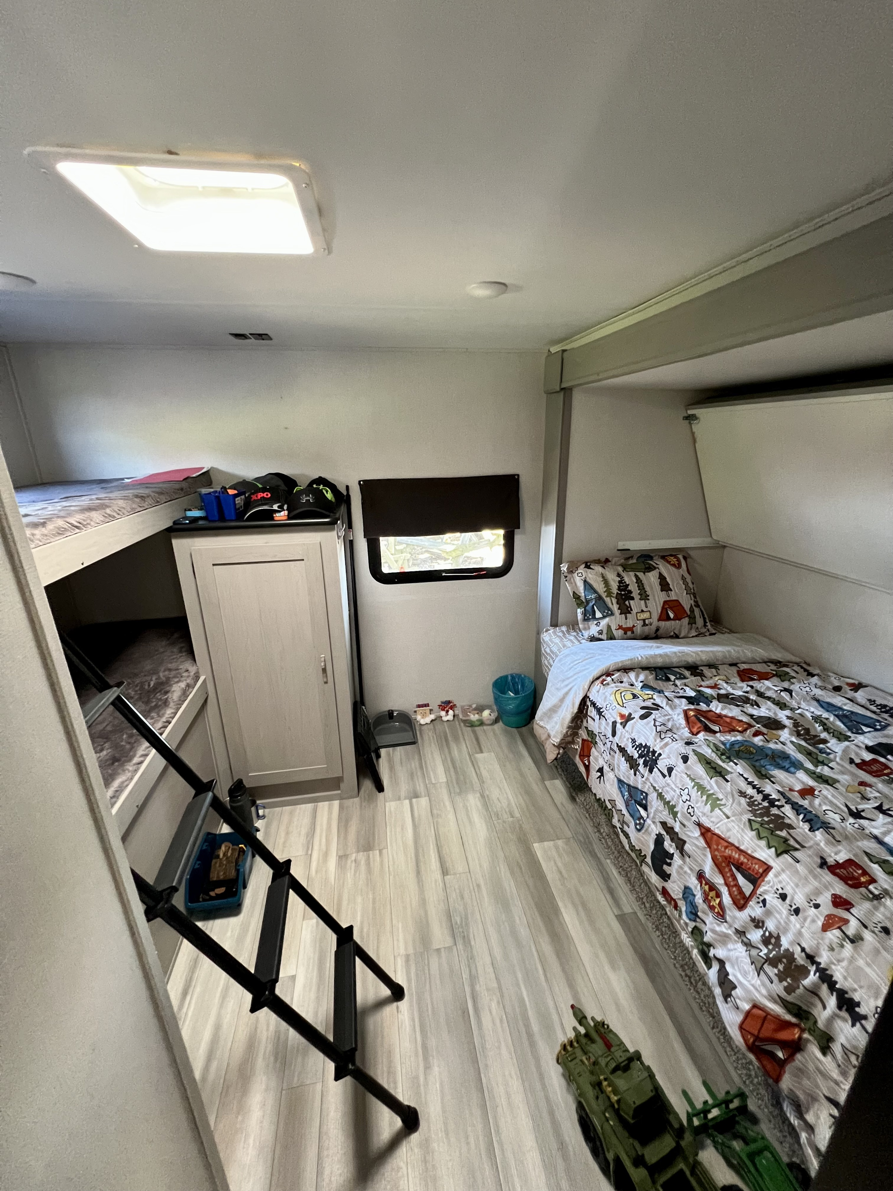 This RV rental bedroom features a bright skylight, bunk beds with a ladder, a cozy single bed, and storage. Ideal for family travel.. Prime Time RV Tracer 2022