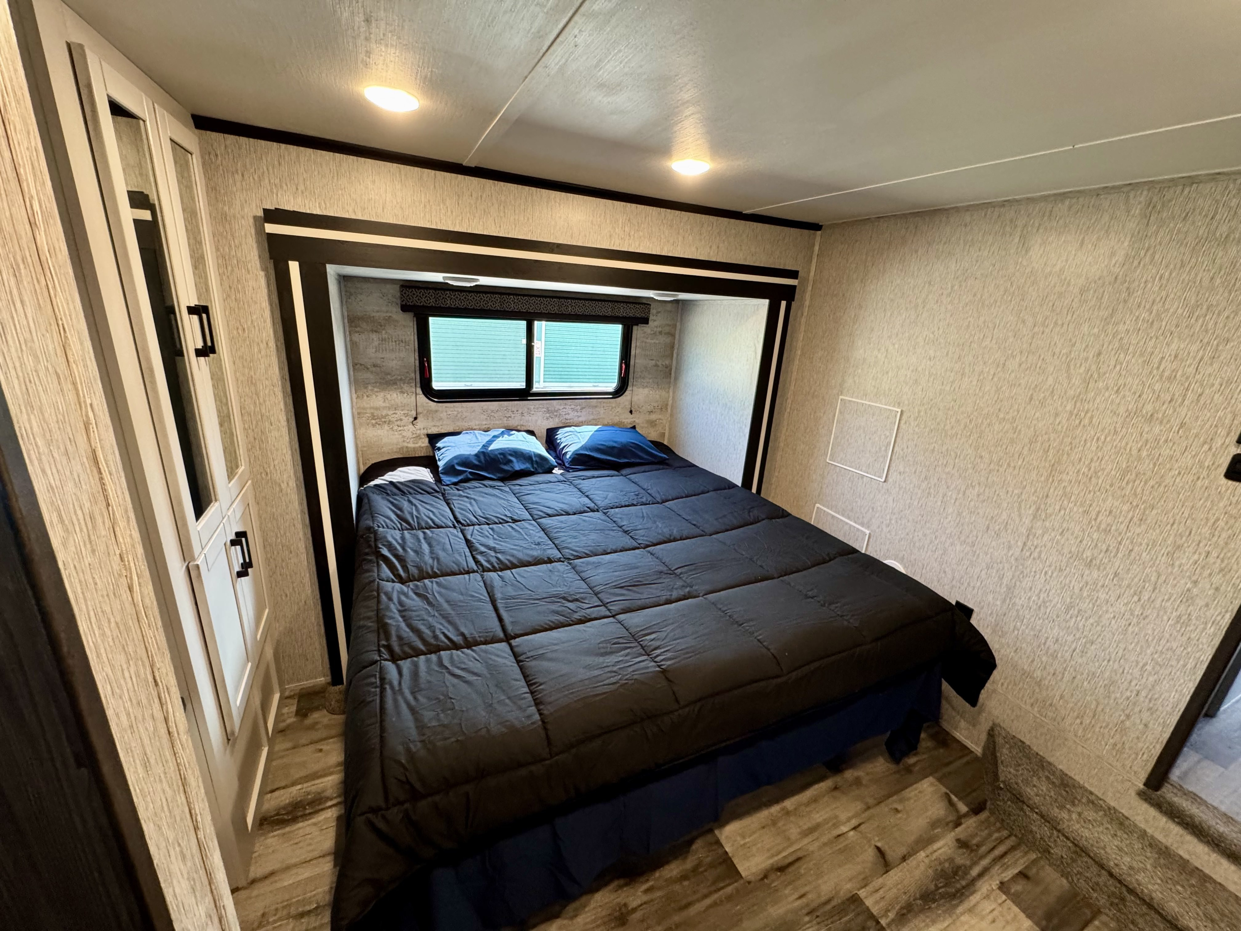 This compact RV rental bedroom offers a comfortable bed, window, and built-in storage, perfect for a relaxing trip.. Crossroads RV Hampton 2023