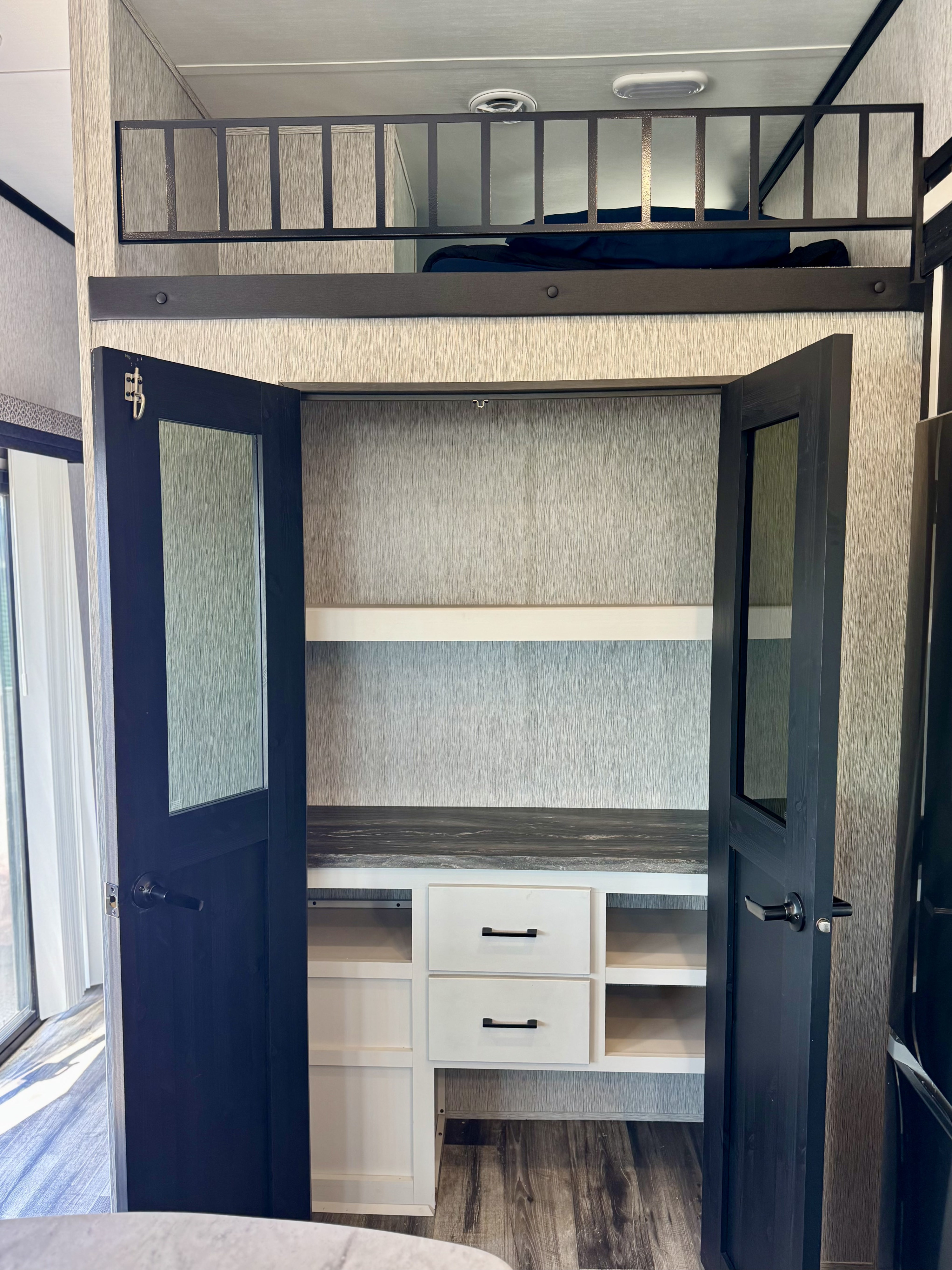 RV rental featuring a loft bed above a functional pantry/closet with shelves, drawers, and dark, paneled doors.. Crossroads RV Hampton 2023