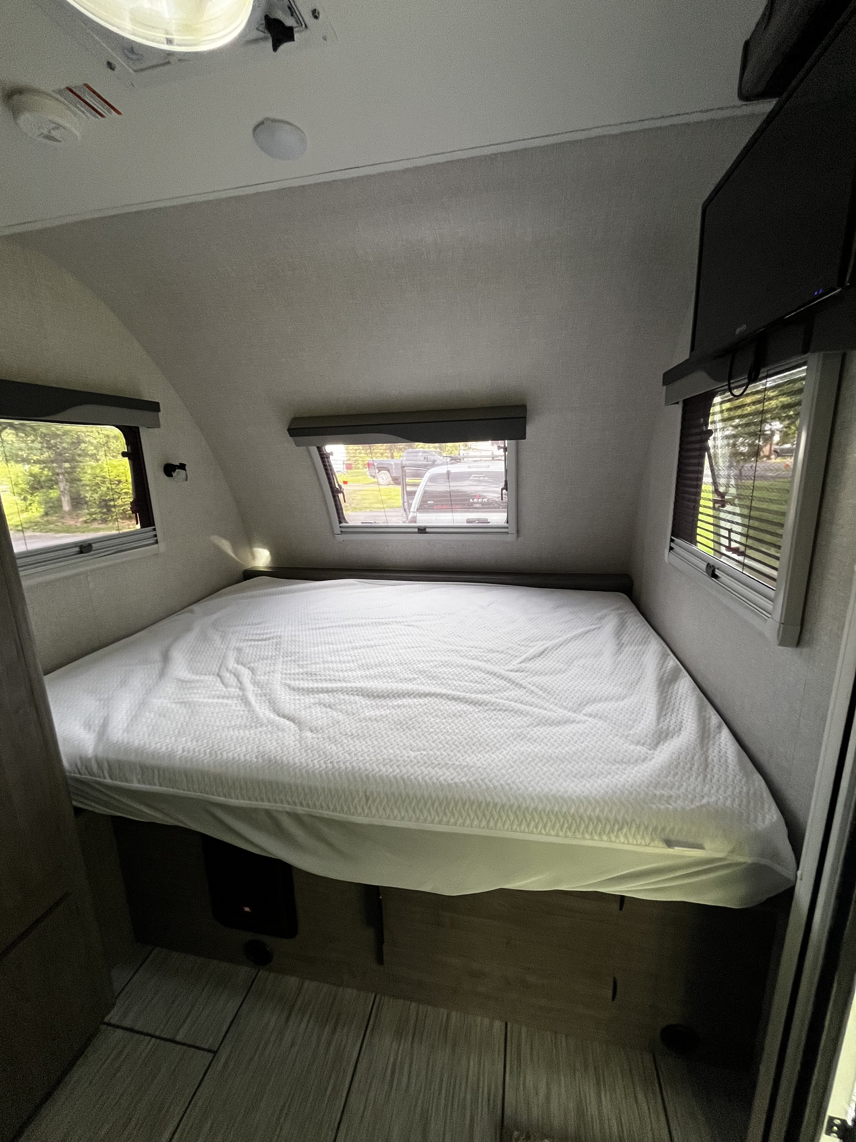 RV rental bedroom: comfortable bed with a white mattress, multiple windows with outdoor views, and a wall-mounted TV.. Lance Manufacturing 1575 2023